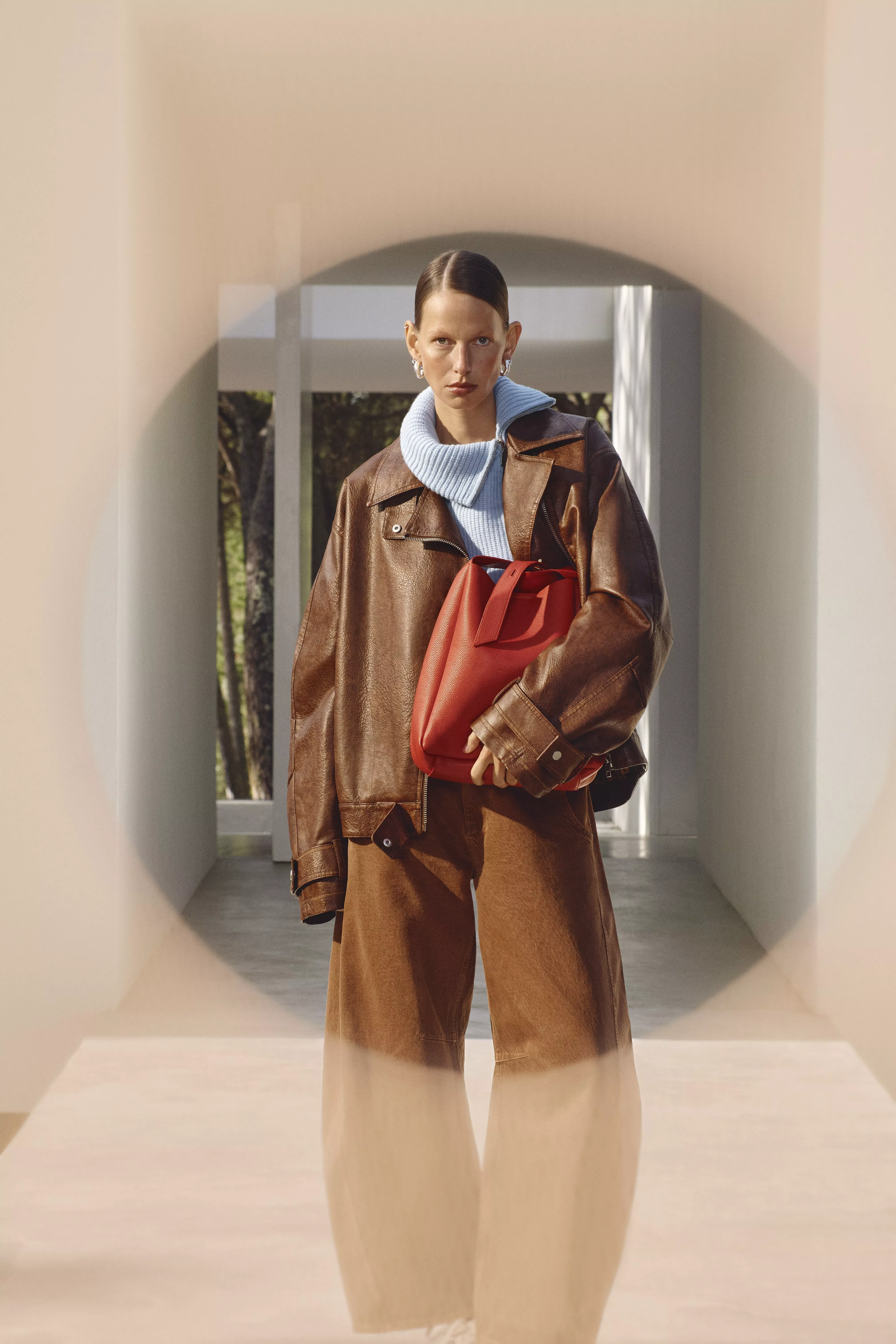woman wearing a brown leather jacket and holding a red bag
