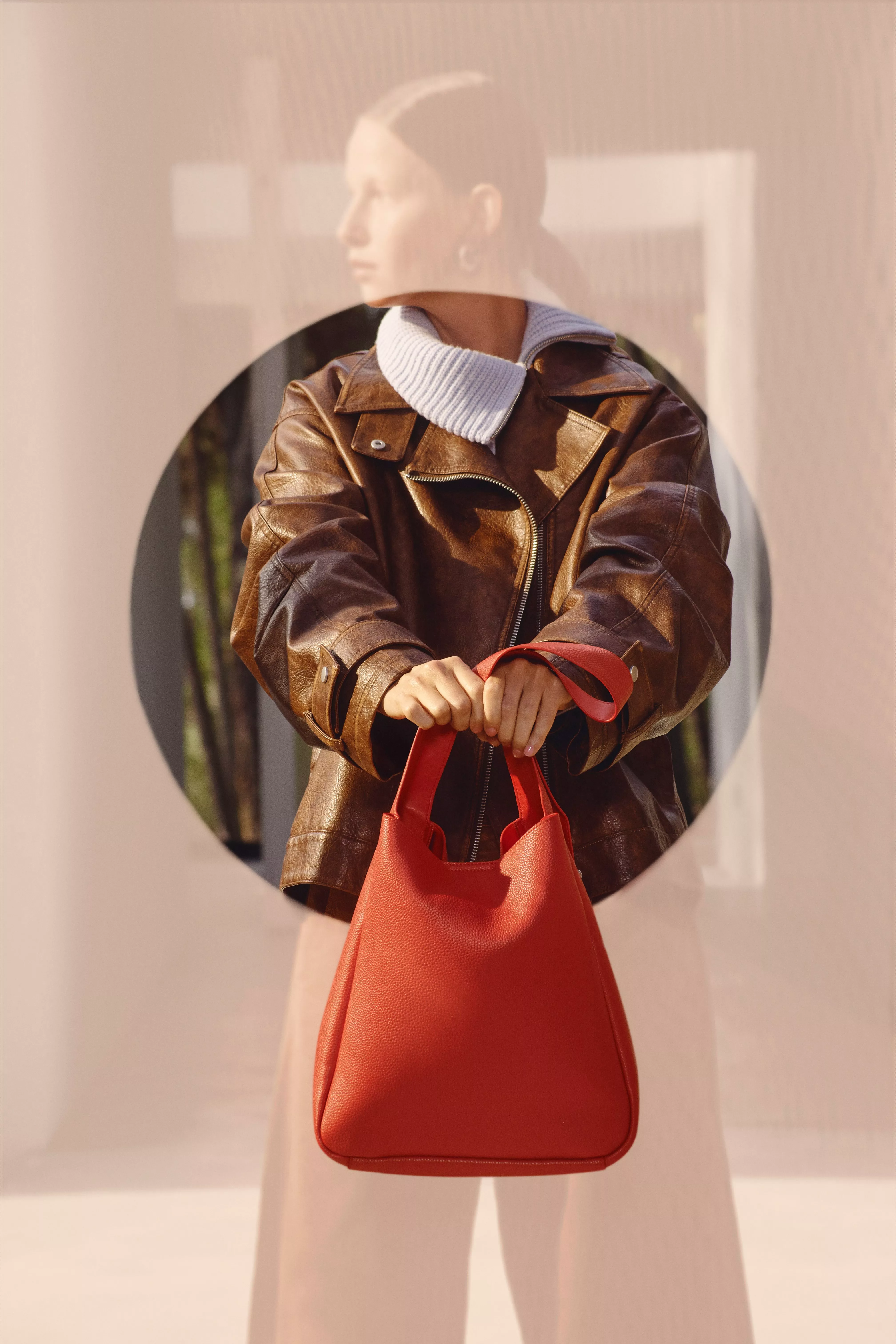 woman wearing a brown leather jacket and holding a red bag