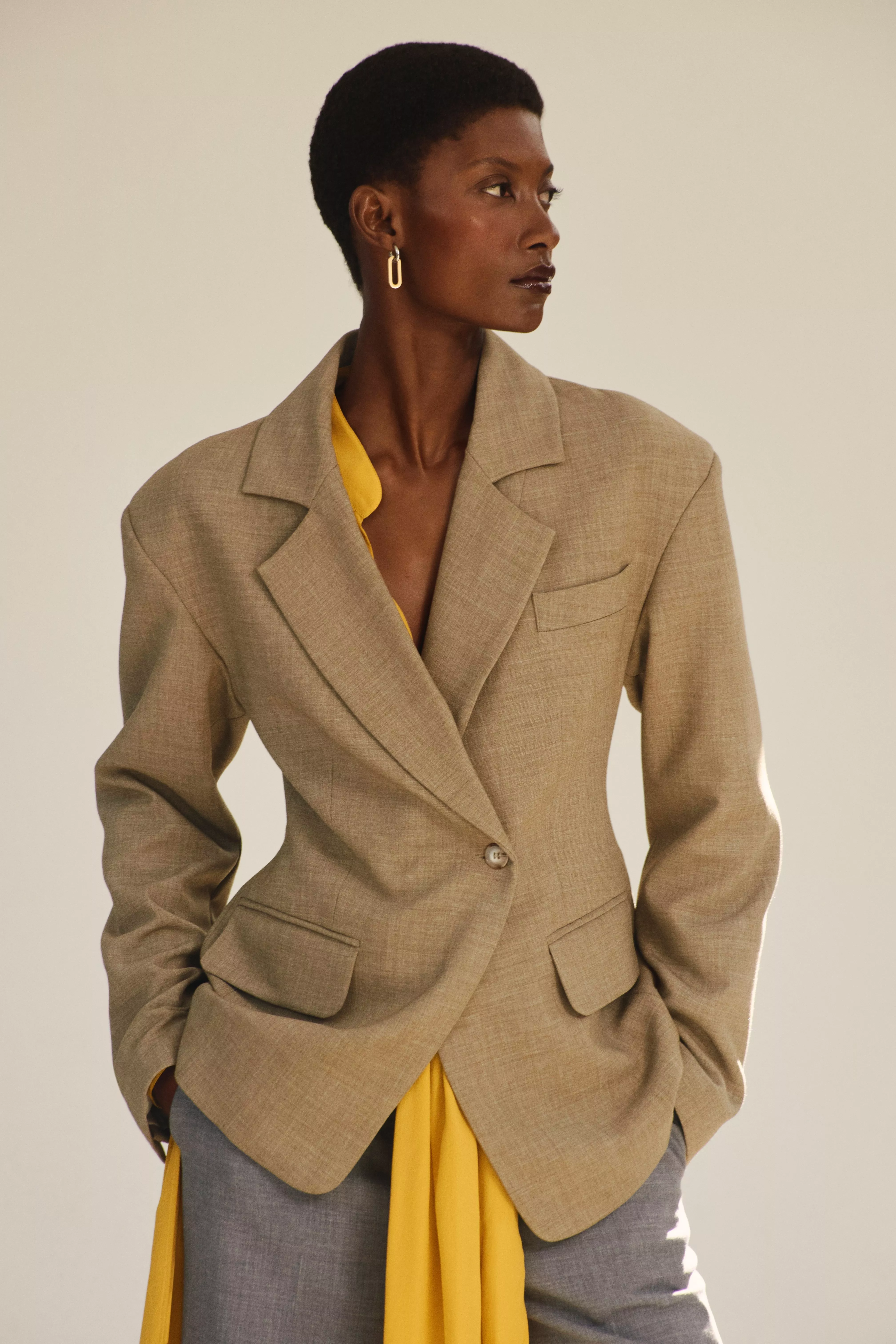A person in a stylish green blazer with matching trousers and flowing shirt stands by the ocean
