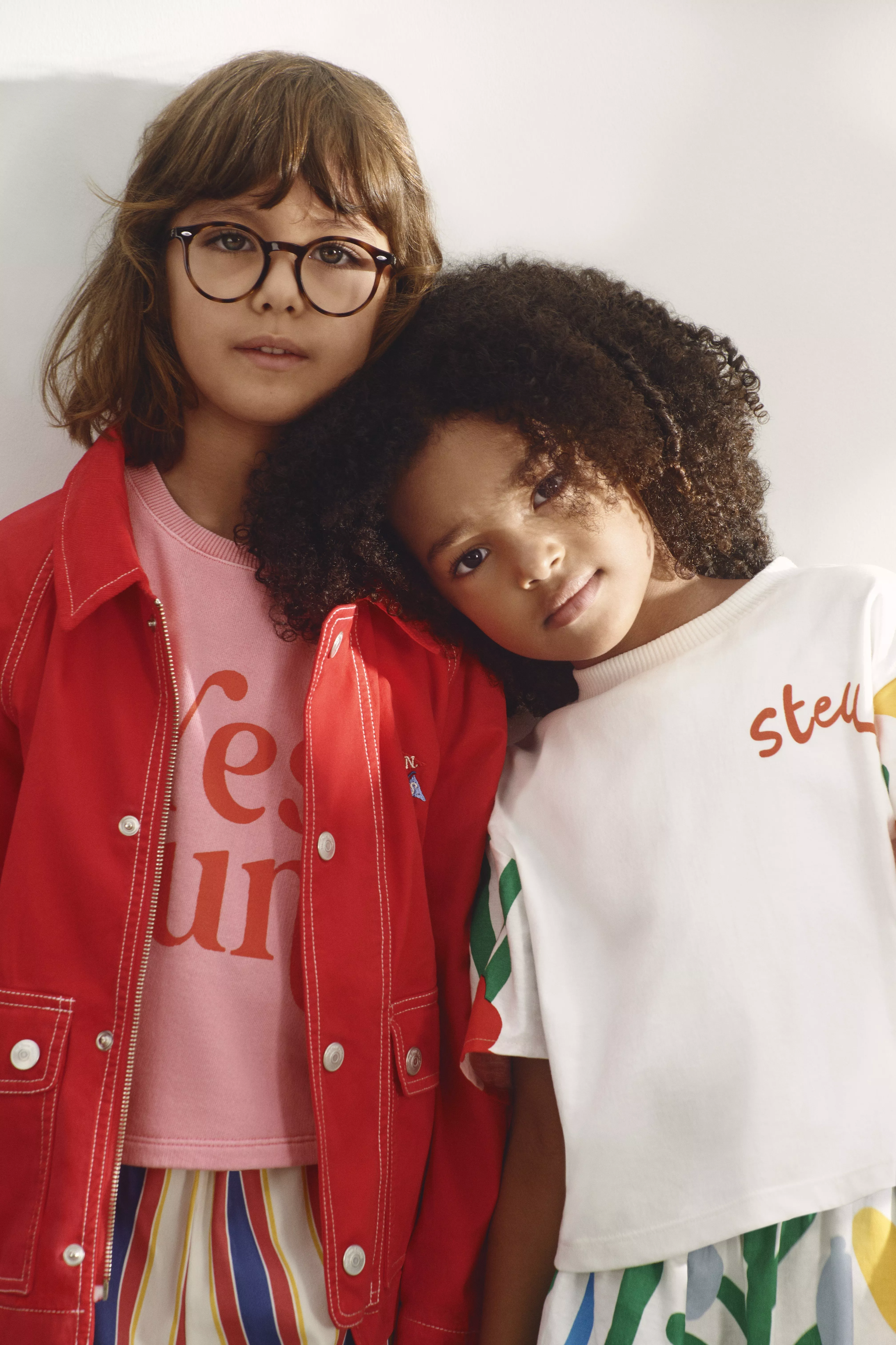 Two children wearing colourful outfits; one in a red jacket, and the other in a striped skirt.