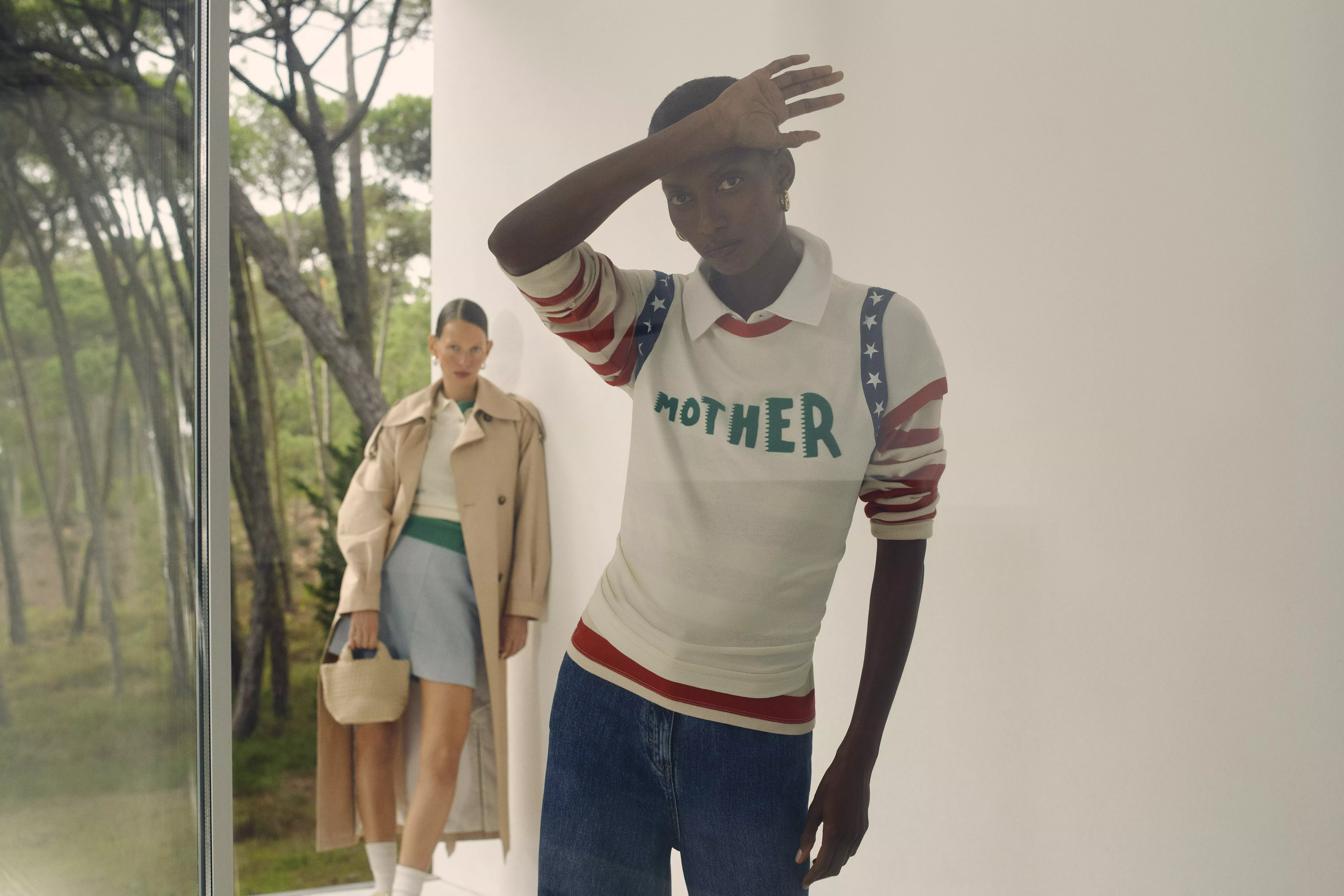 A model wearing a white top with "MOTHER" branding across the front, with blue and red accents, and blue jeans