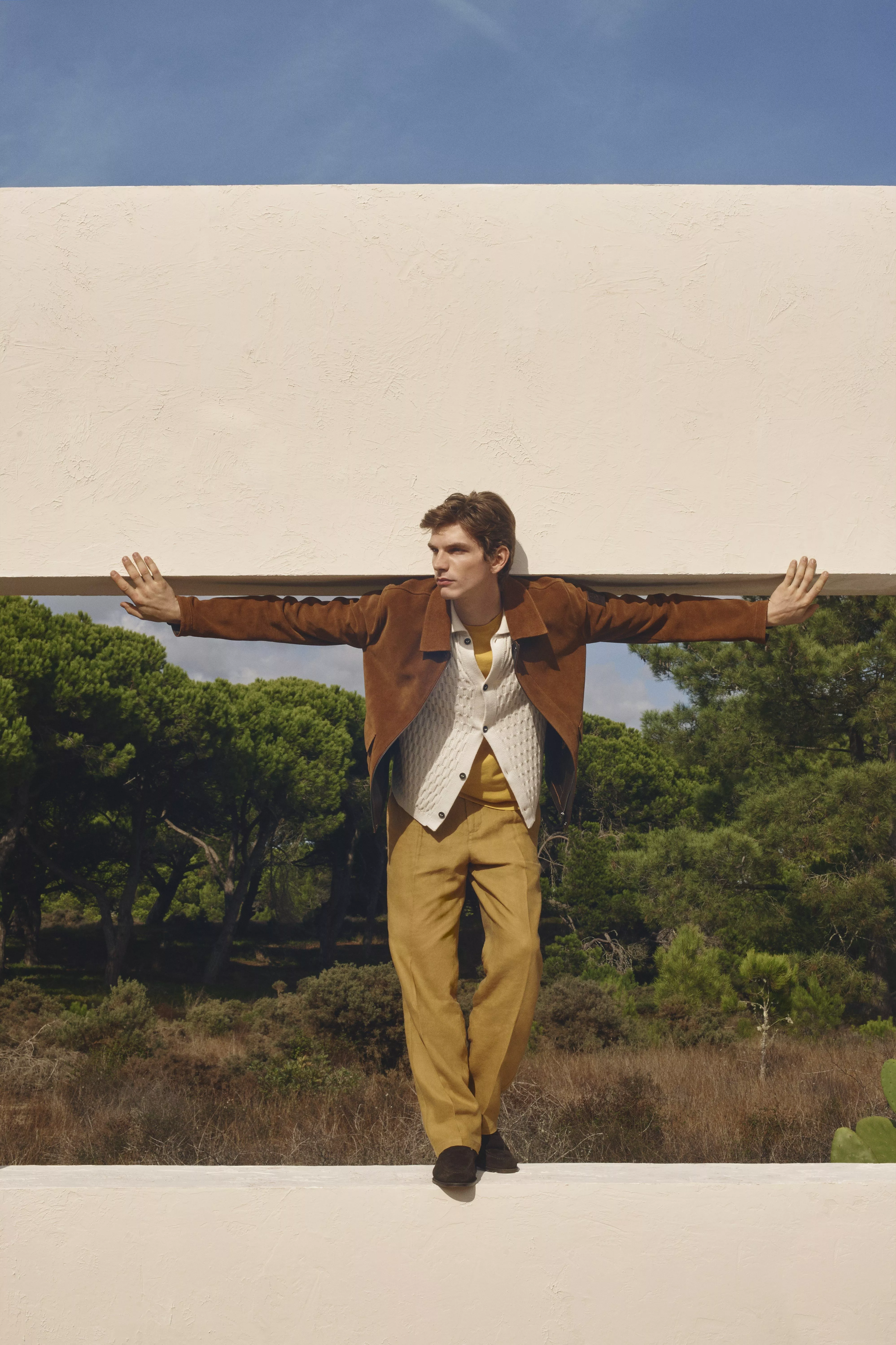 Man wearing mustard trousers, cream button up cardigan and tan suede jacket