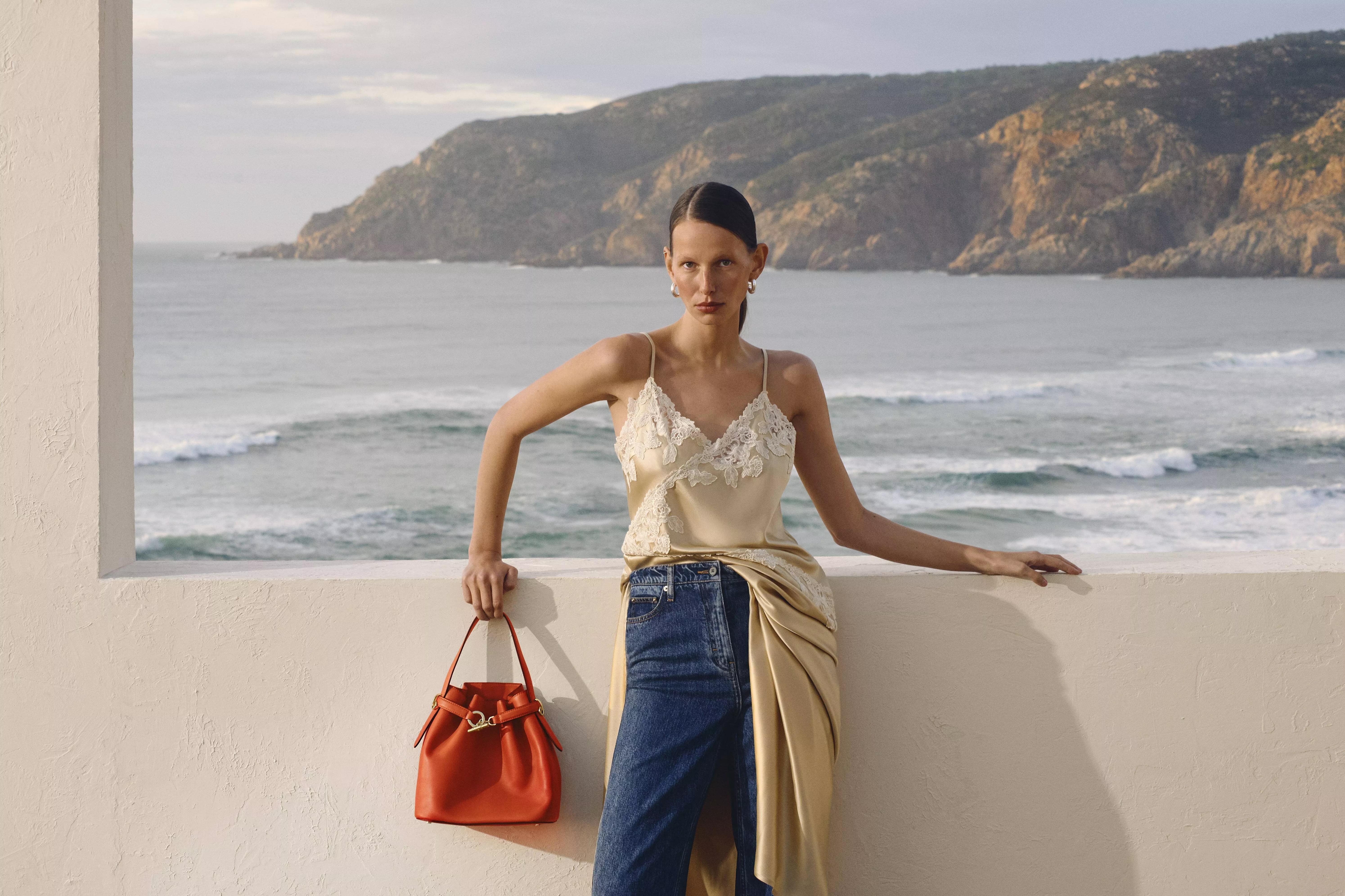 Two people stand in a forest framed by a large beige window, wearing casual summer outfits.