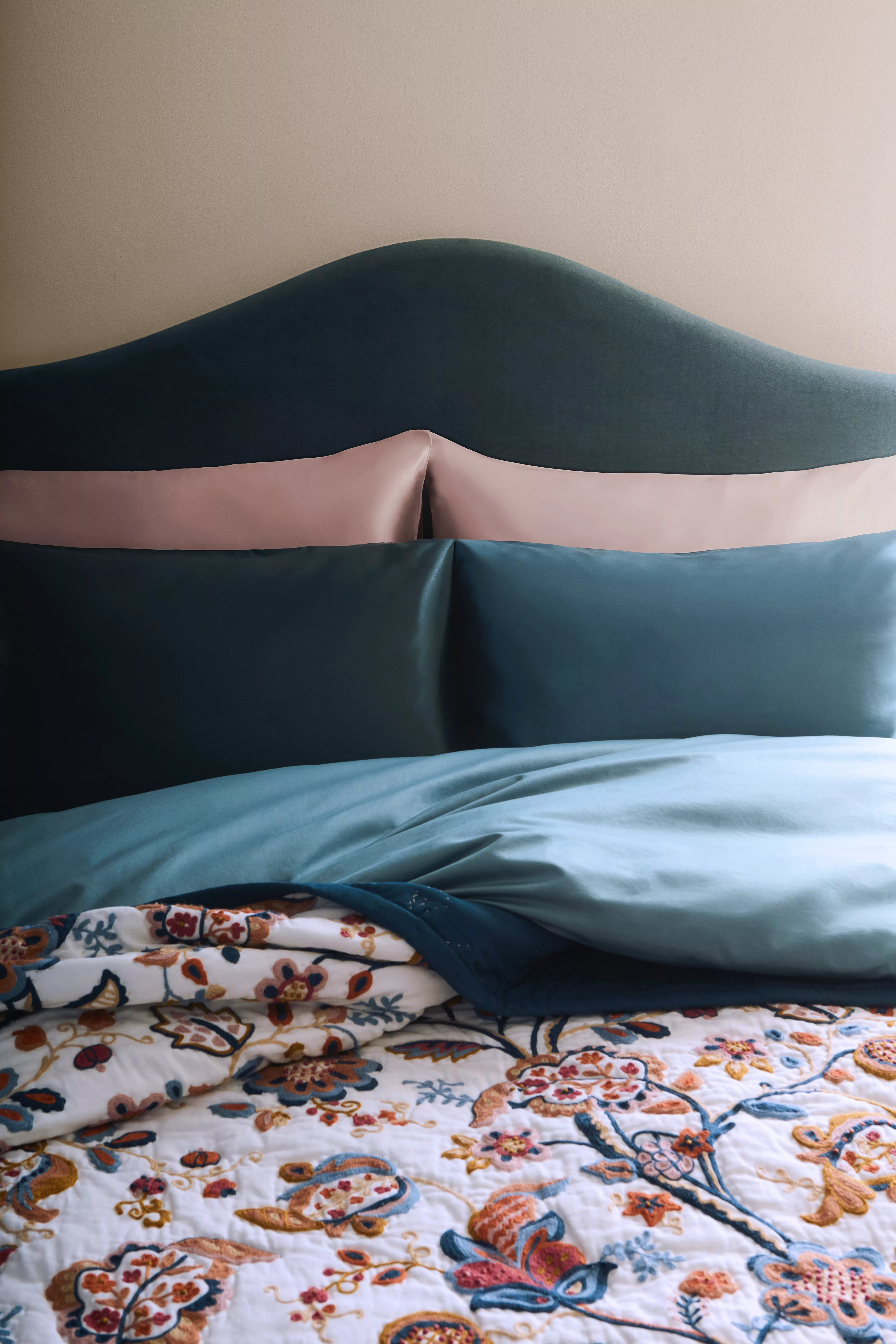 Teal upholstered headboard with blue duvet and floral quilt, modern bedroom bedding in soft natural light