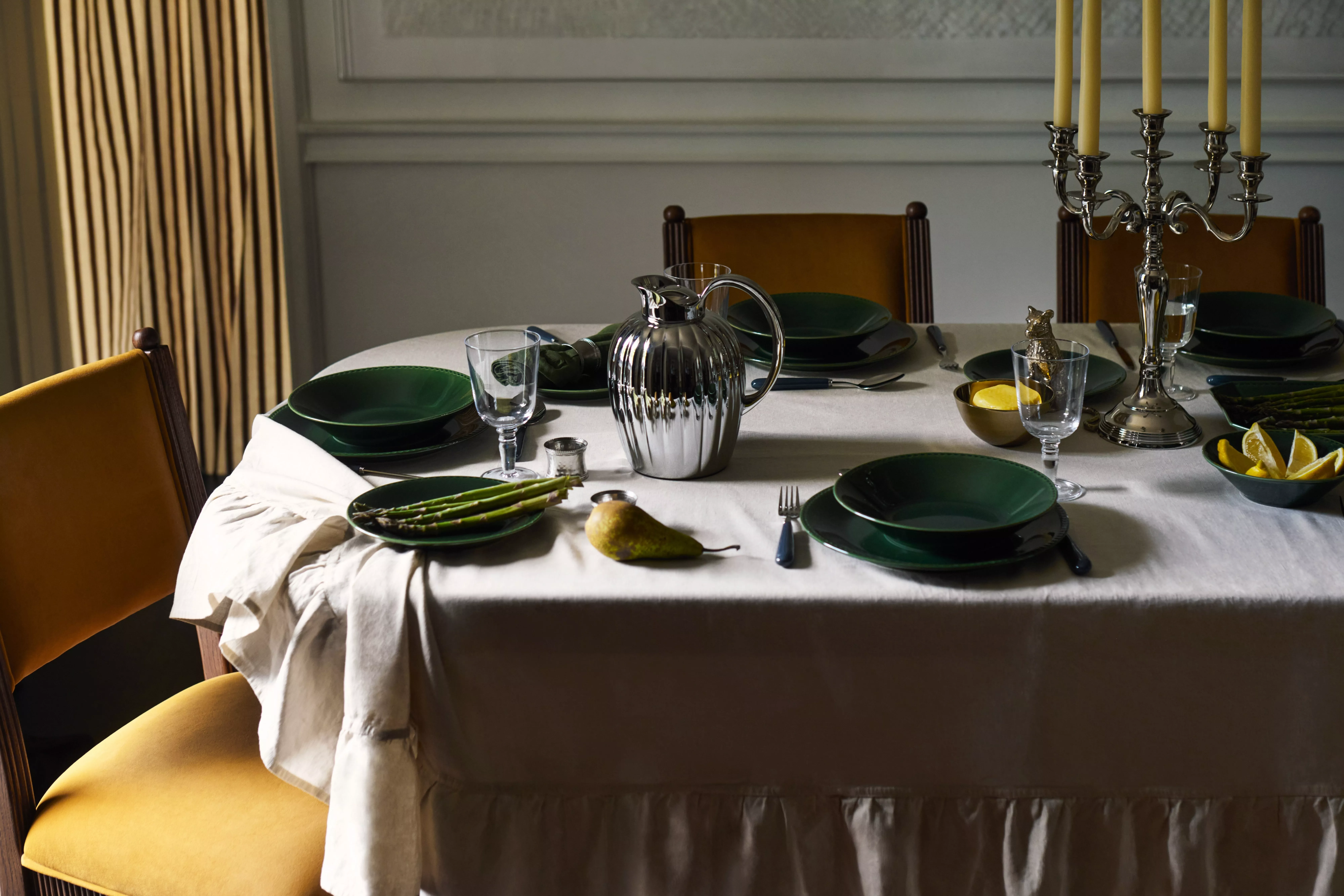 Elegant dining table set with green plates, silver jug, asparagus and candles in a classic dining room