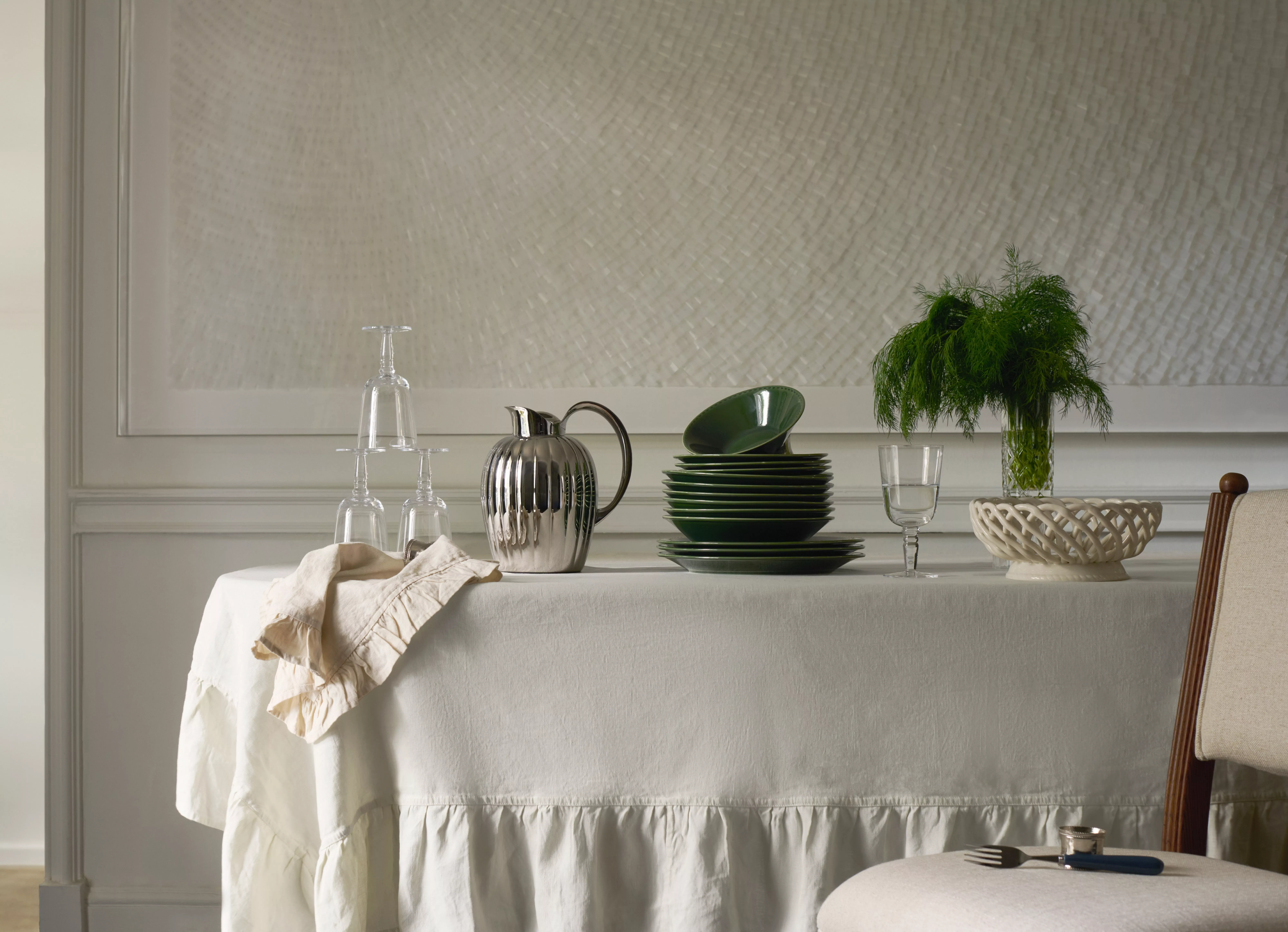 Elegant dining table setting with green plates, silver jug, glassware and vase of foliage on linen cloth