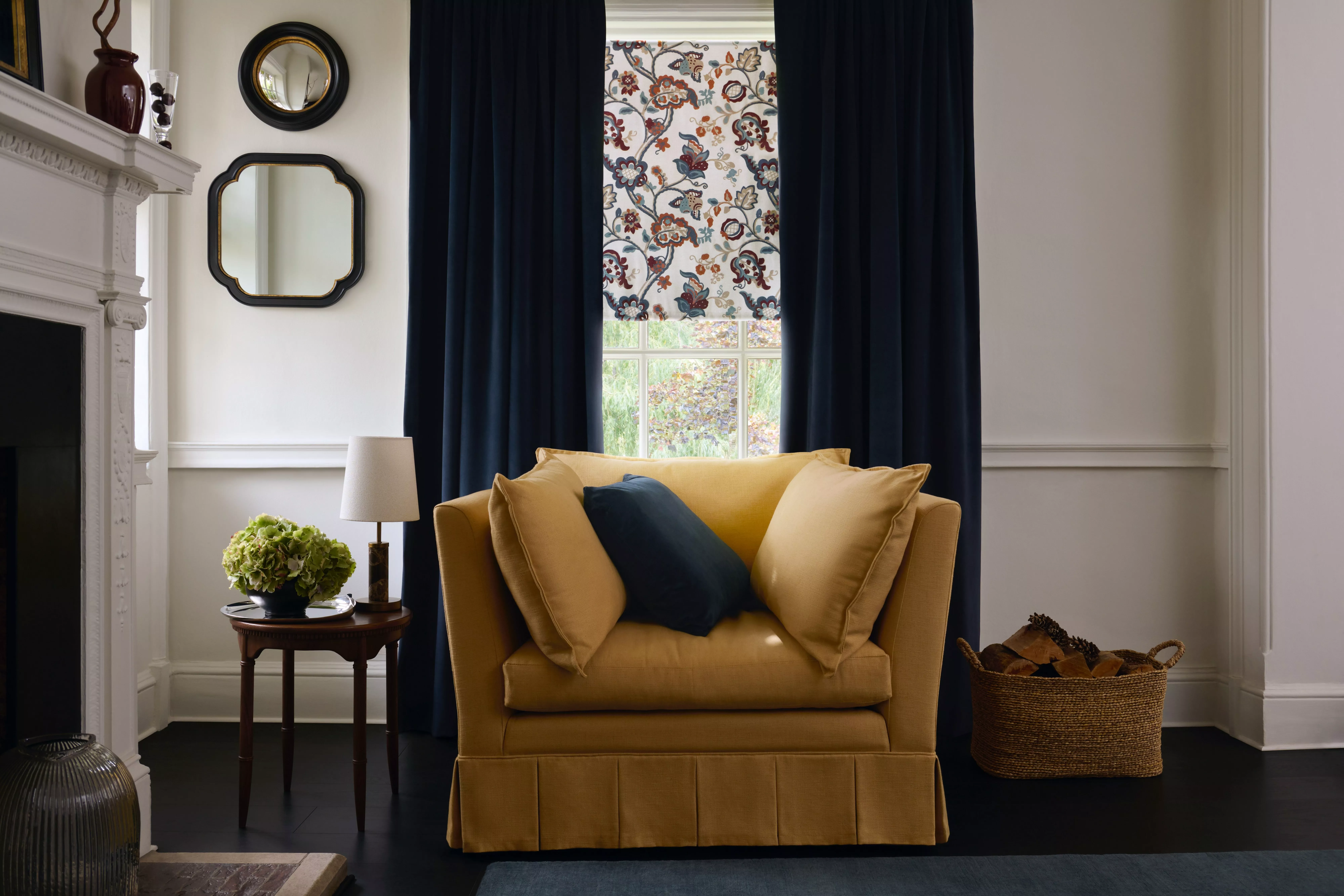 Cosy living room with mustard armchair, navy curtains, floral blind, side table lamp and mirrors on wall