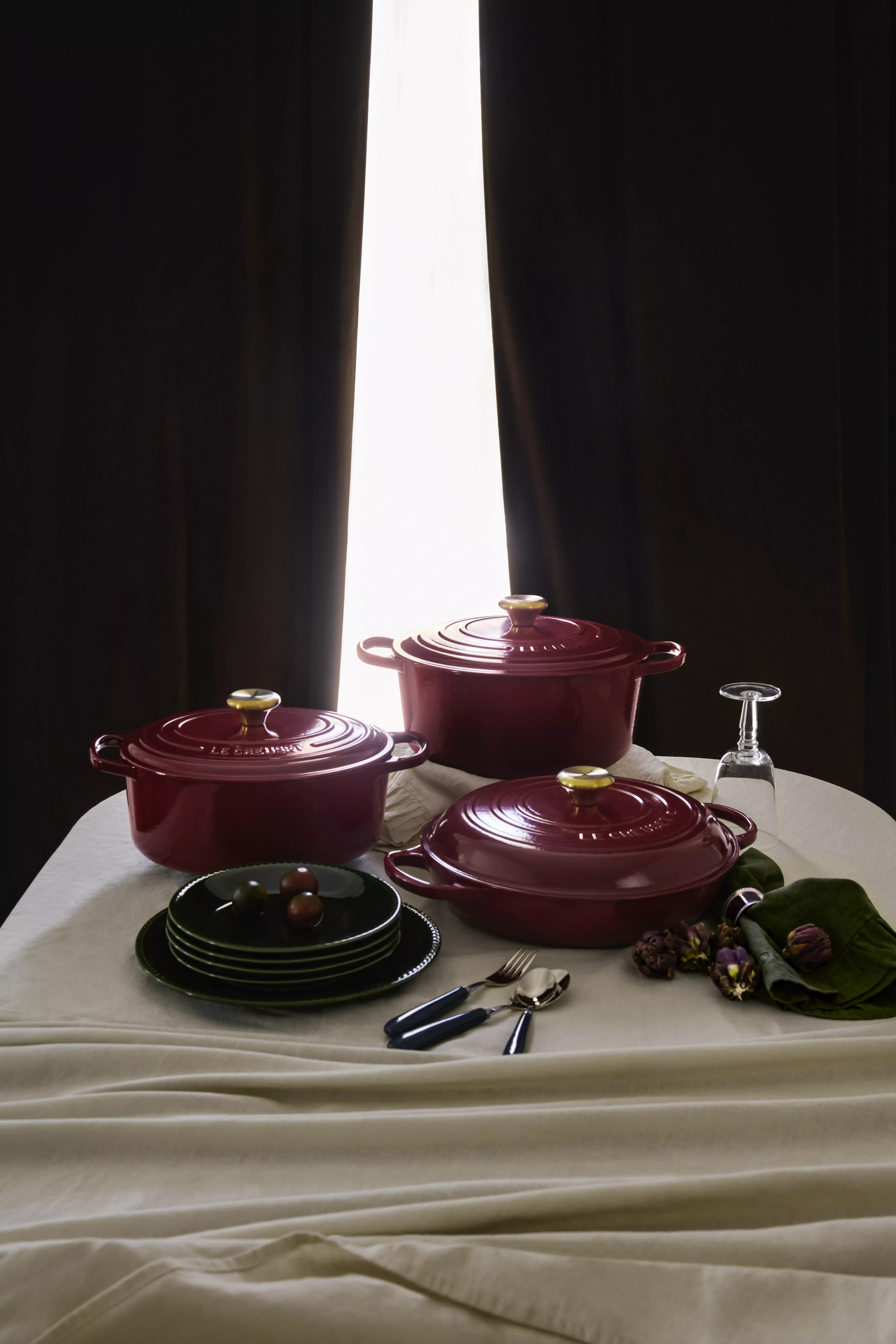 Burgundy cast iron casserole dishes on a table with plates, cutlery and glass, styled for kitchen cookware SEO