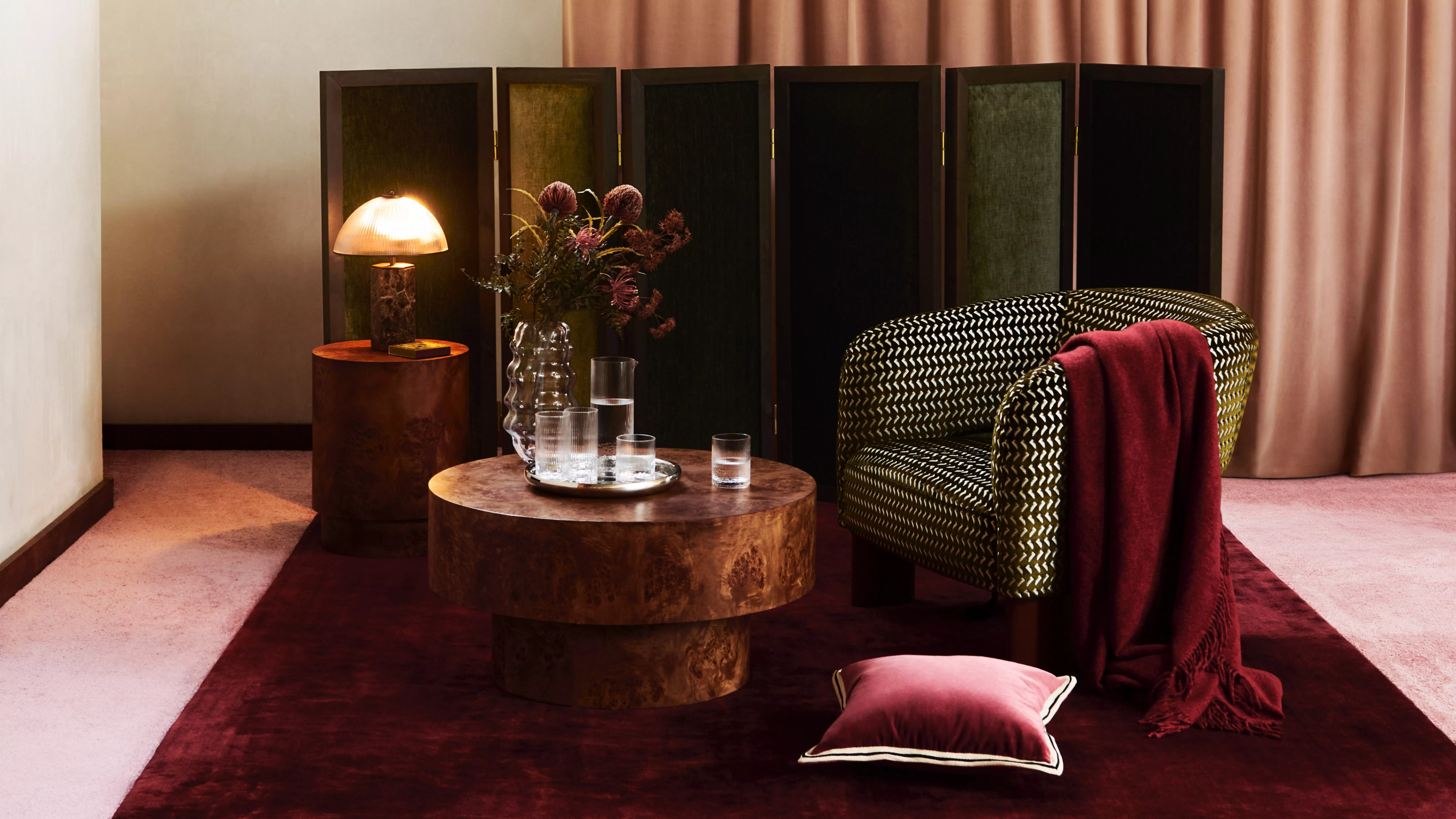 Luxury living room interior with patterned armchair, wooden coffee tables, warm lamp and burgundy rug.