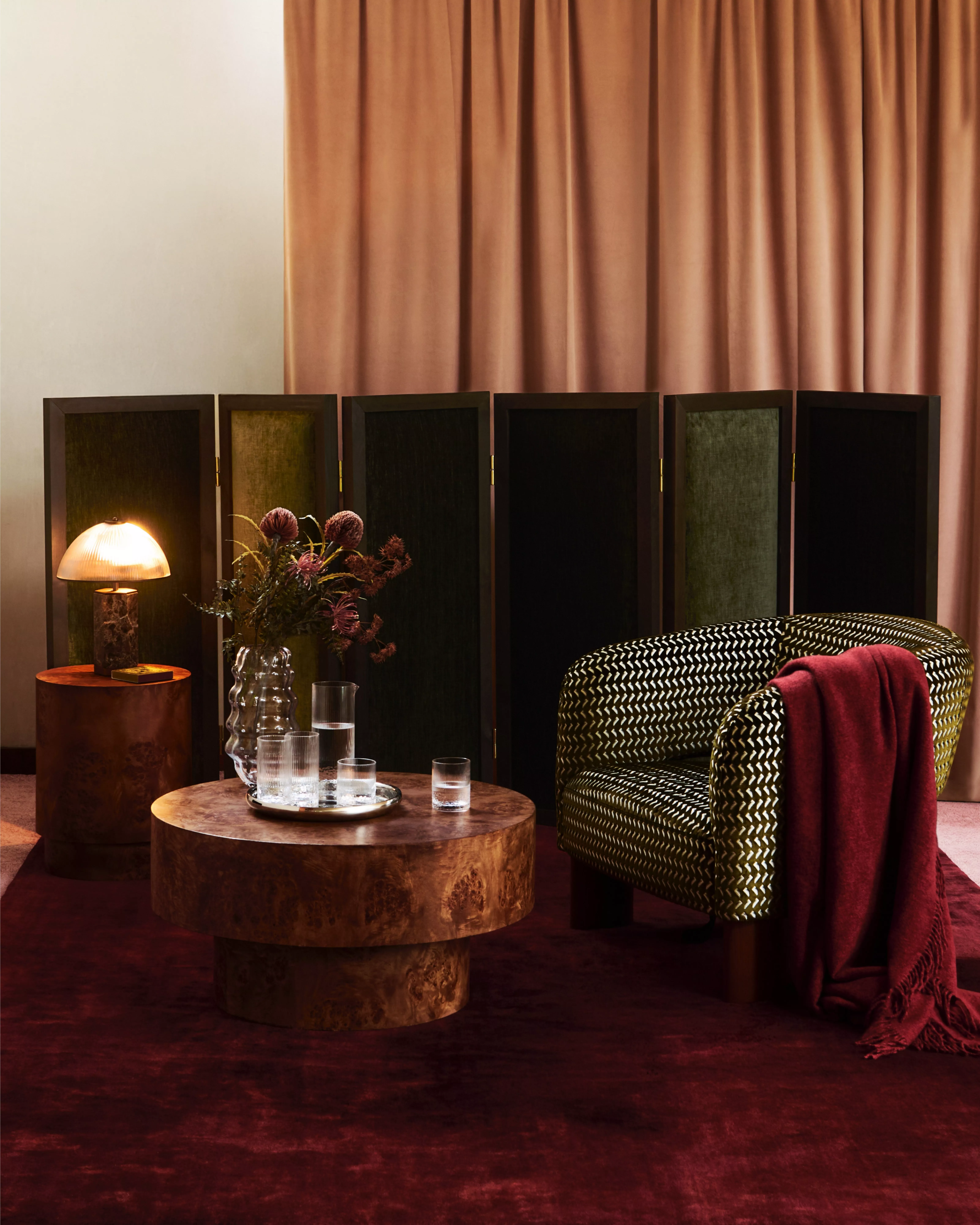 Modern lounge interior with patterned armchair, burgundy throw, round wooden coffee table and soft lamp lighting