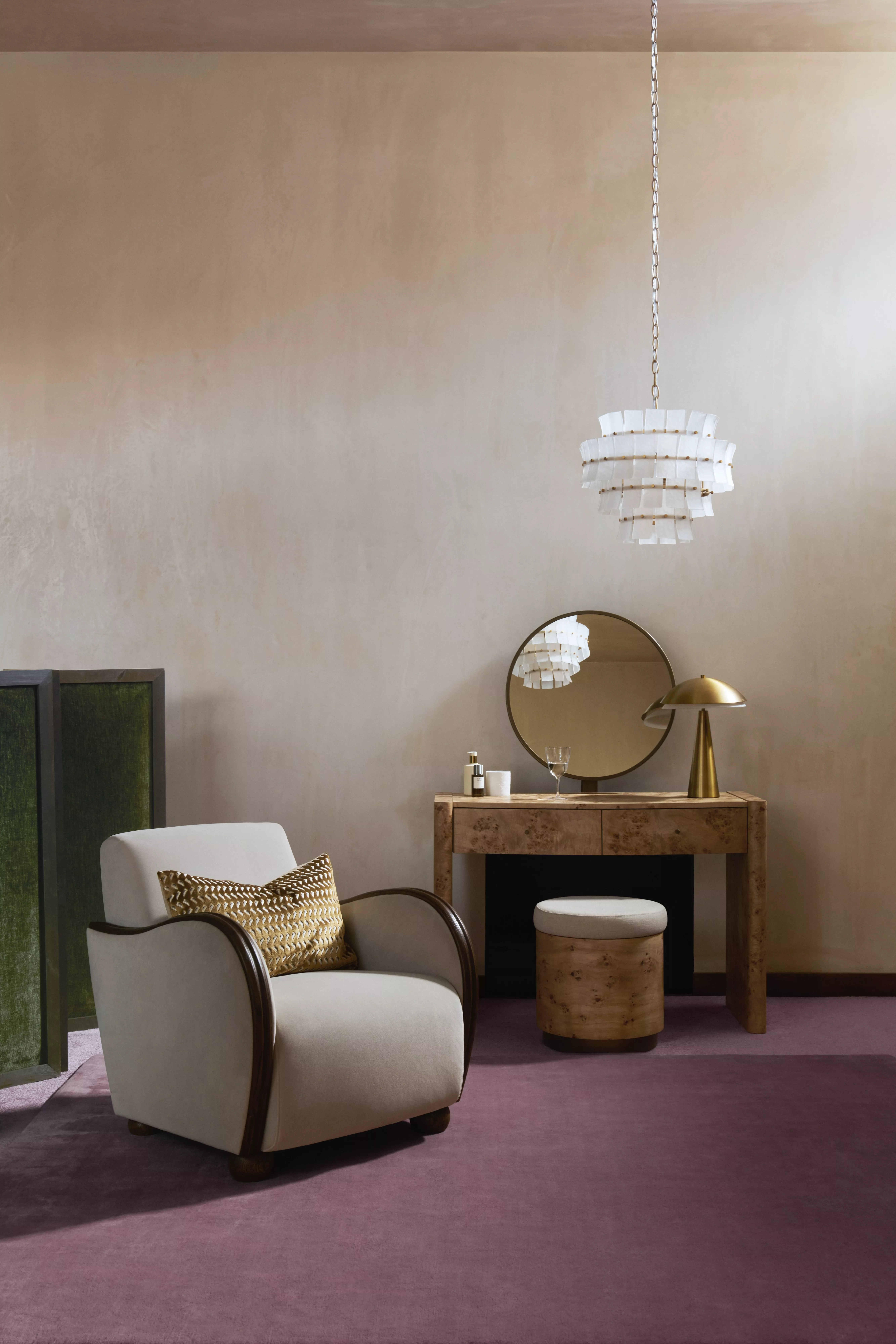 Modern bedroom dressing area with wooden vanity, round mirror, brass lamp, armchair and pendant light