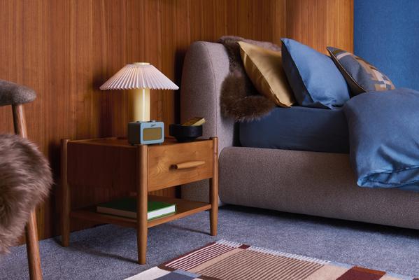 Mid-century modern bedroom with wooden bedside table, pleated lamp and blue cushions on upholstered bed