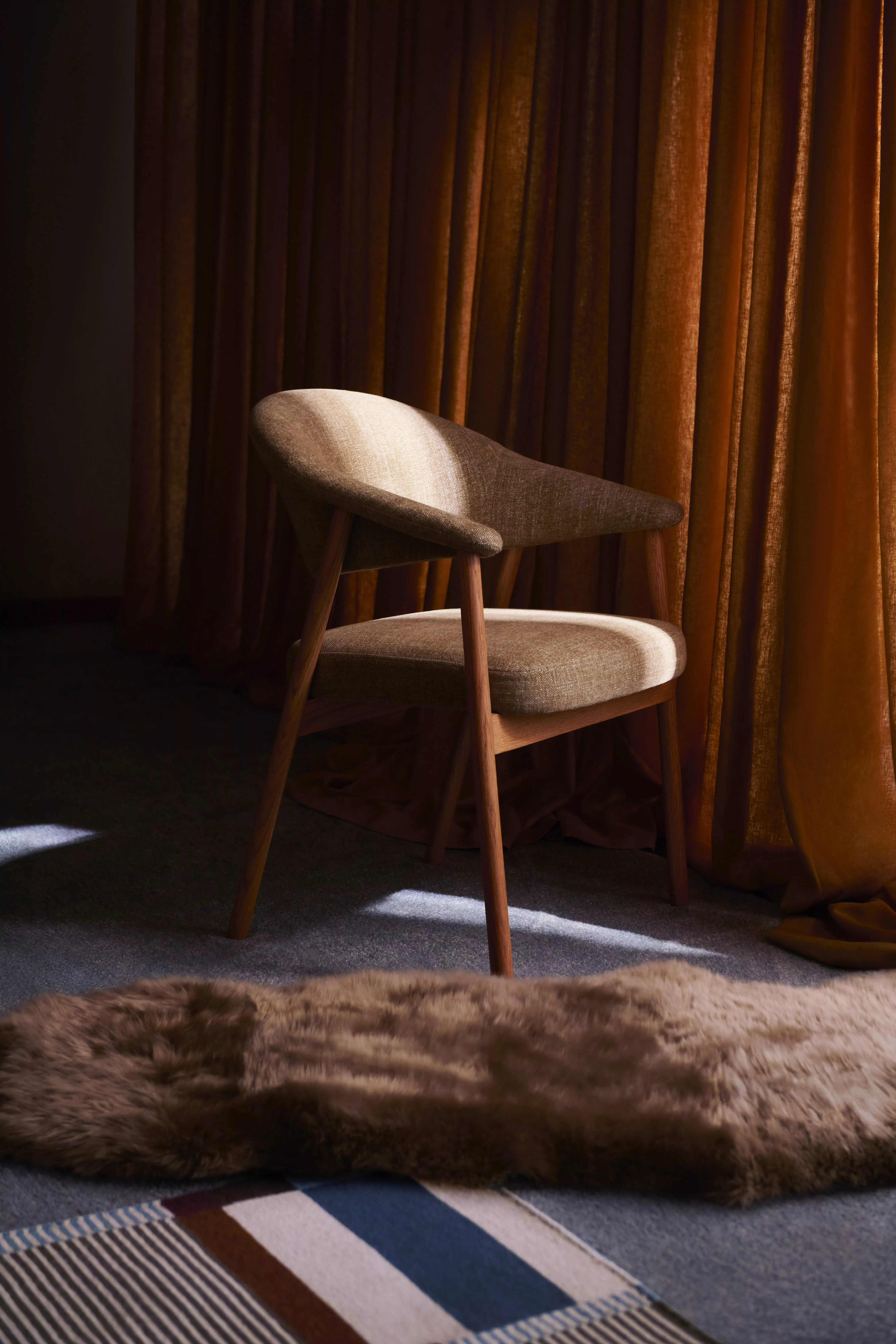 Mid-century modern upholstered wooden armchair in warm light, set against bronze curtains and a soft rug