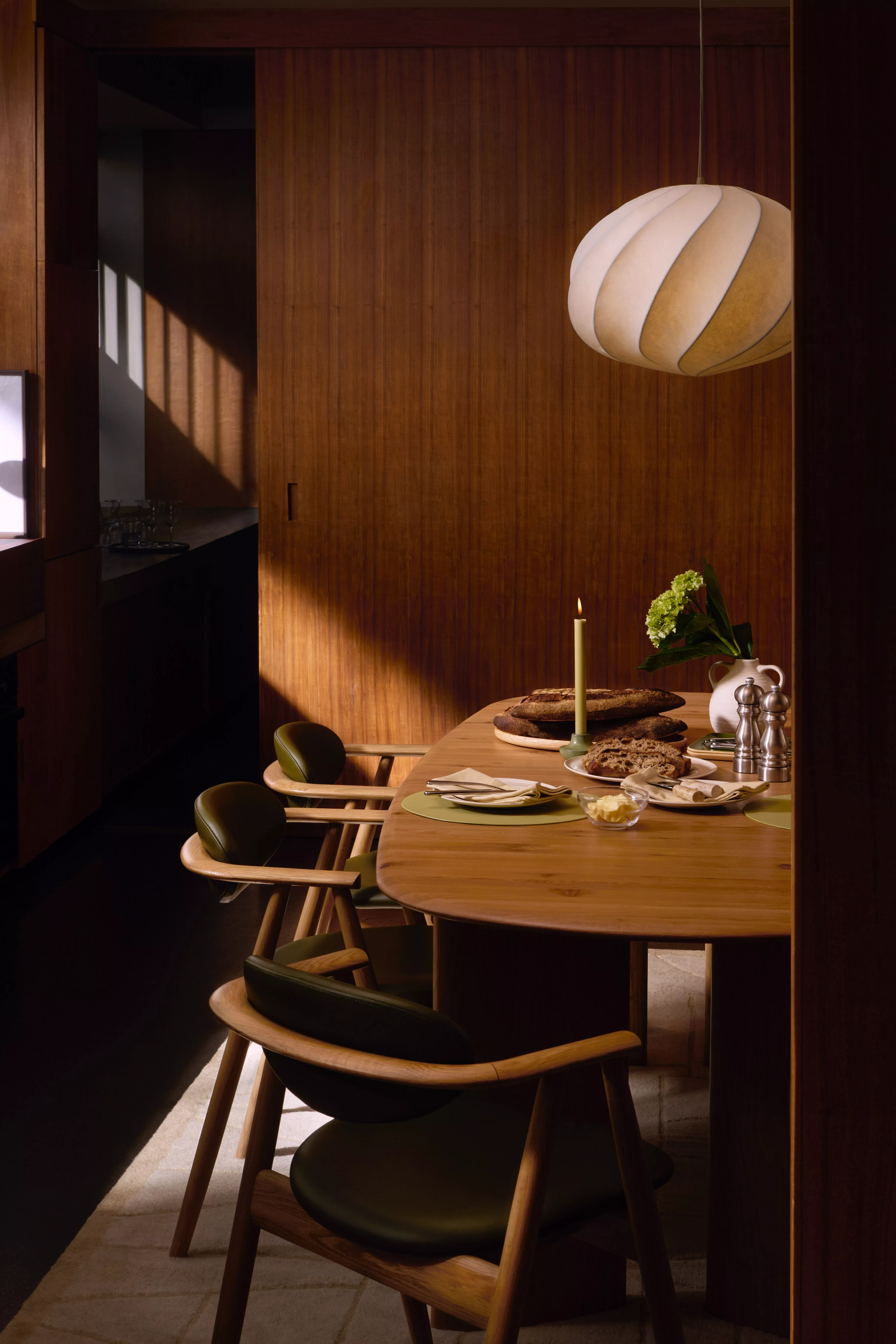 Warm modern dining room with wooden table, green chairs, pendant lamp, candle and rustic bread setting