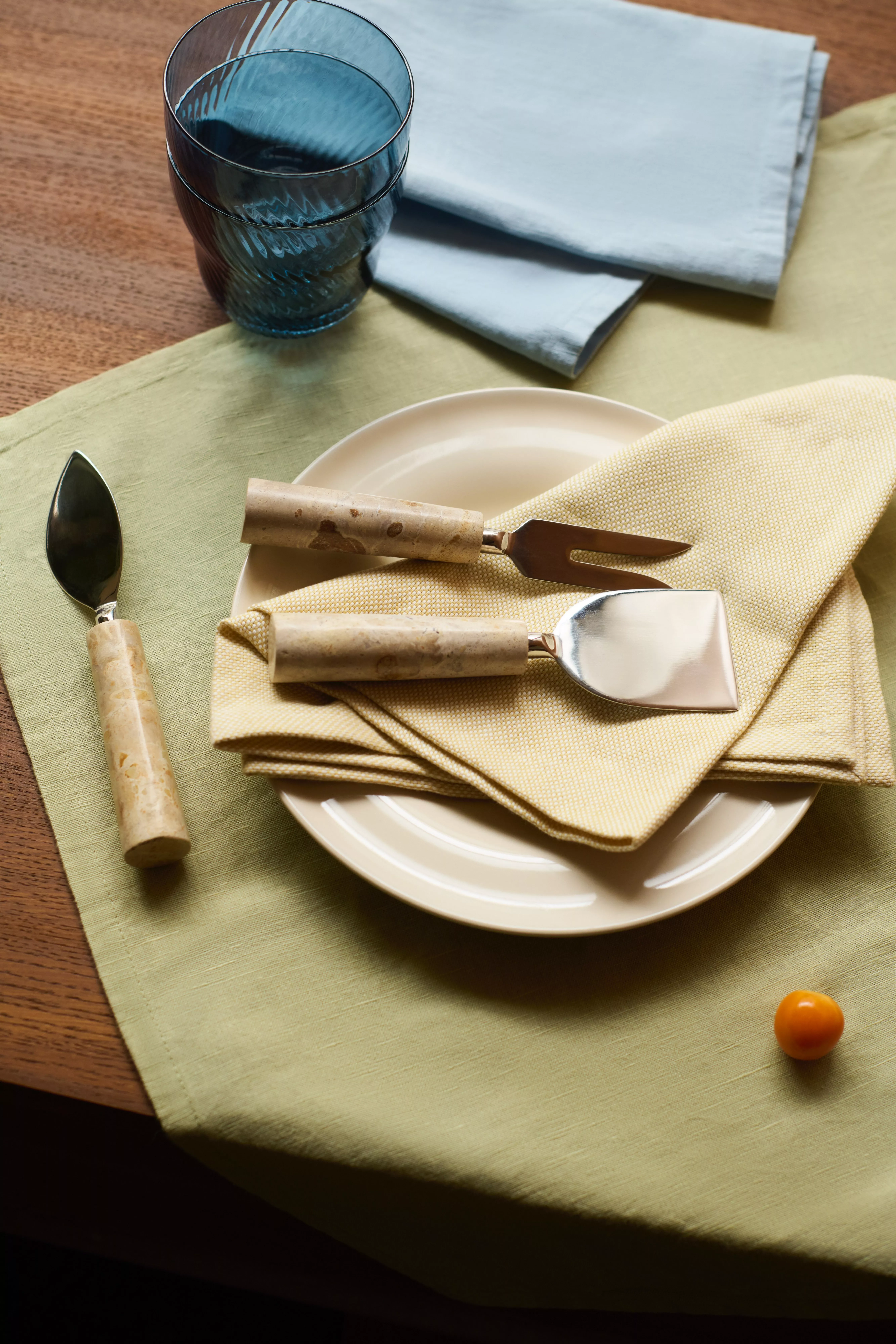 Rust napkin with black cutlery beside blue plates on woven placemat, with glassware on striped tablecloth