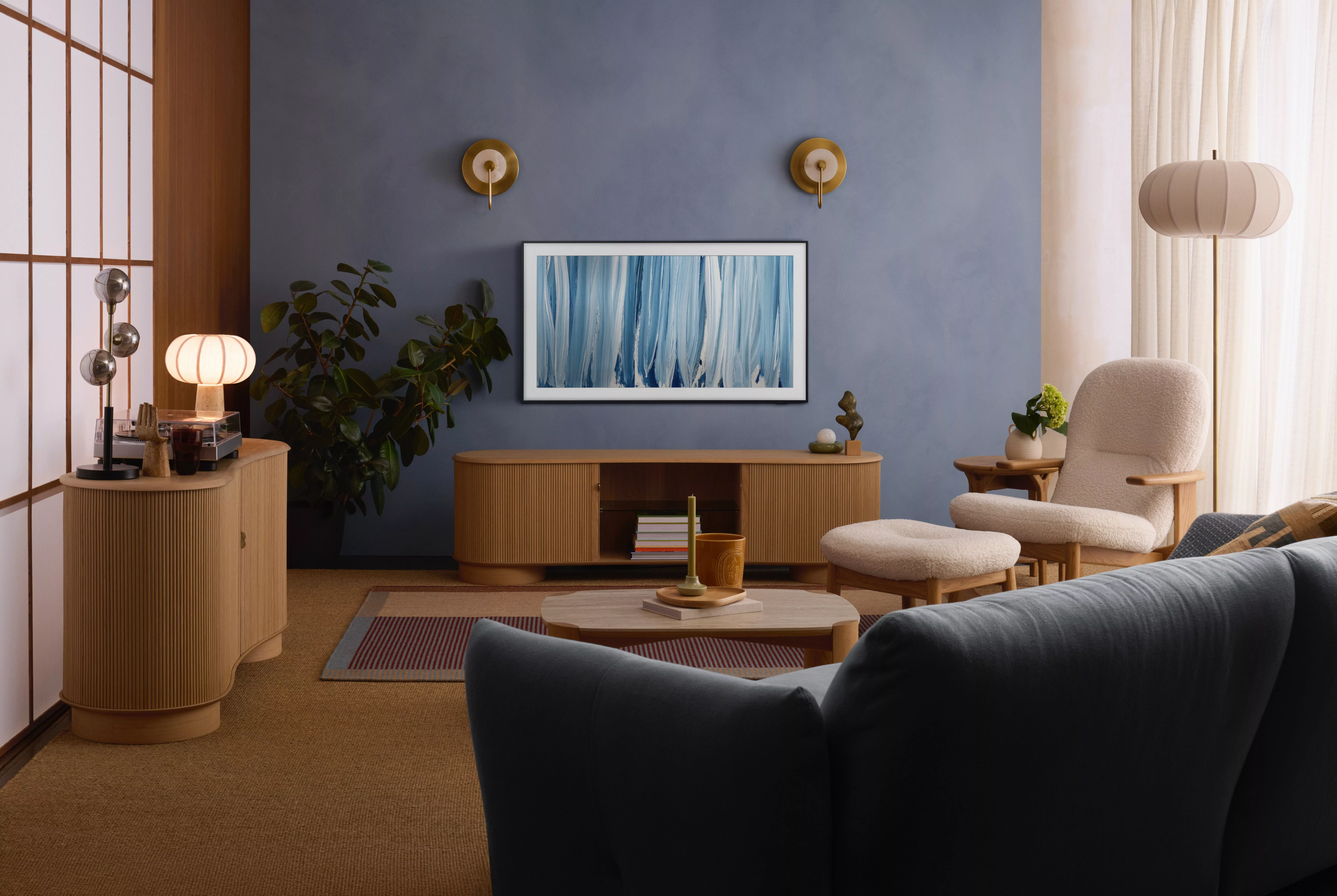 Modern living room with blue feature wall, wooden sideboard, abstract art, cosy armchair and soft lighting