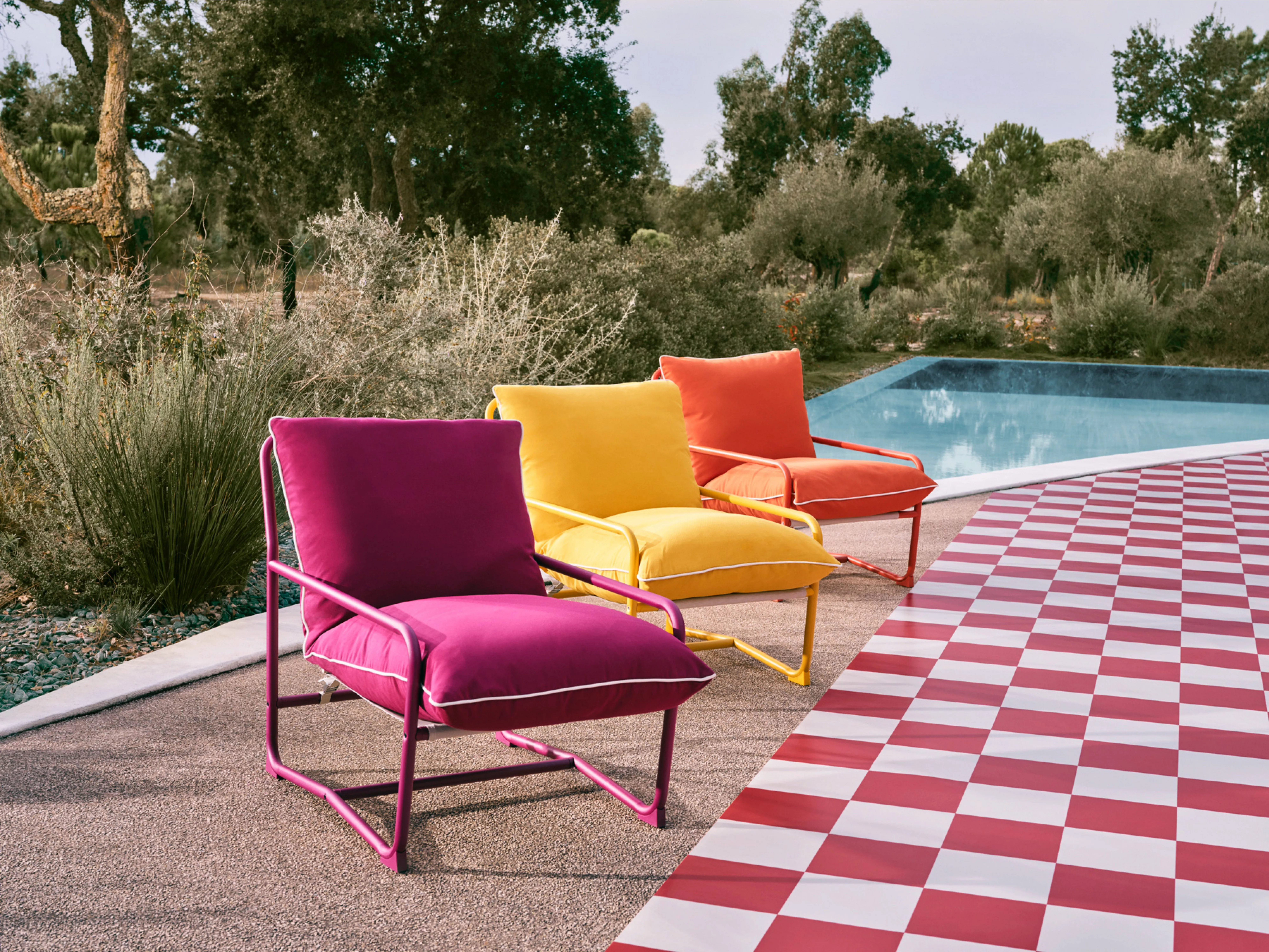Colourful outdoor lounge chairs by a swimming pool with red and white checkered patio flooring in garden setting