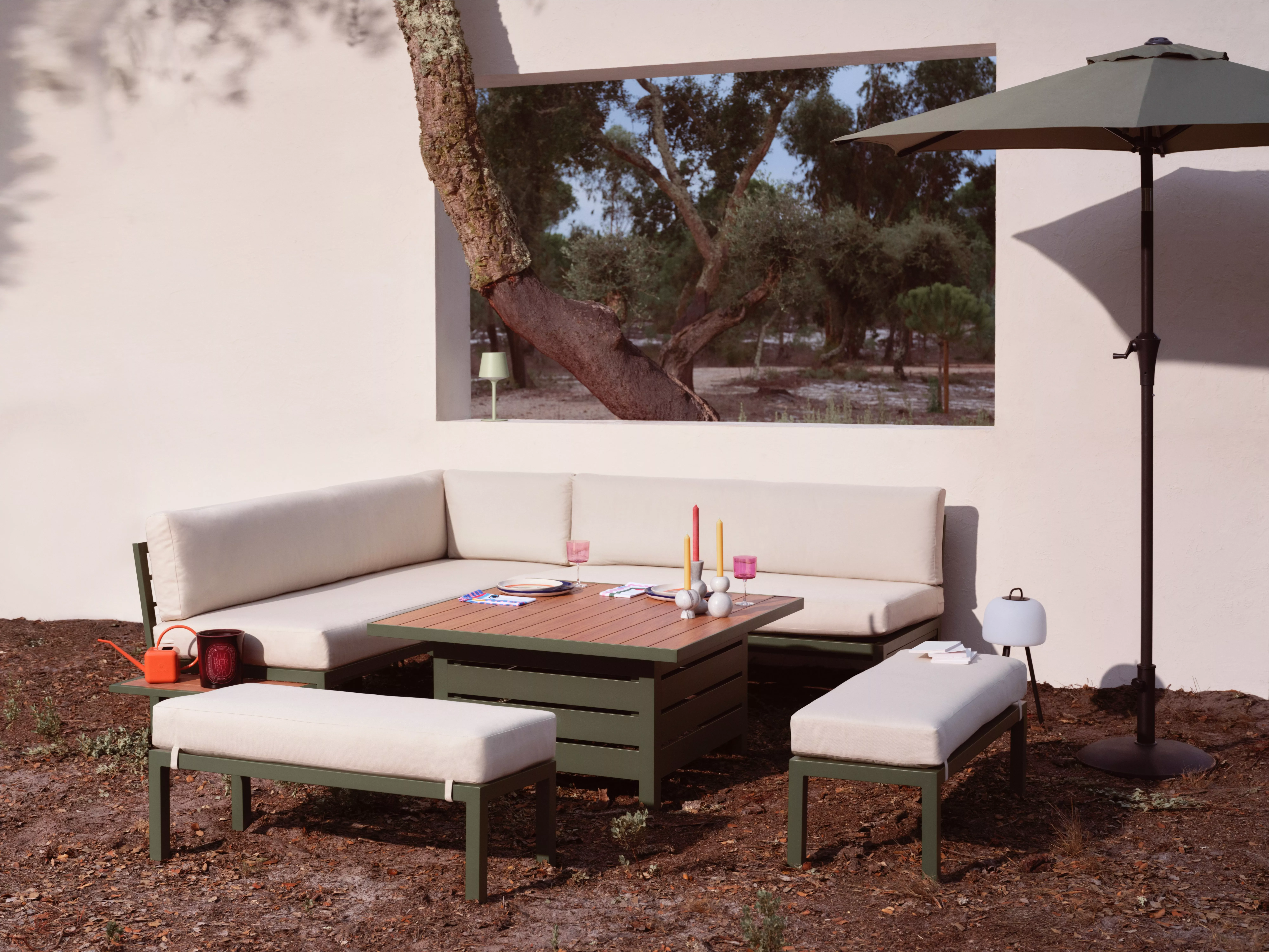 Outdoor patio with a modern L-shaped sofa, wooden table, and benches. An umbrella and decor enhance the setting.