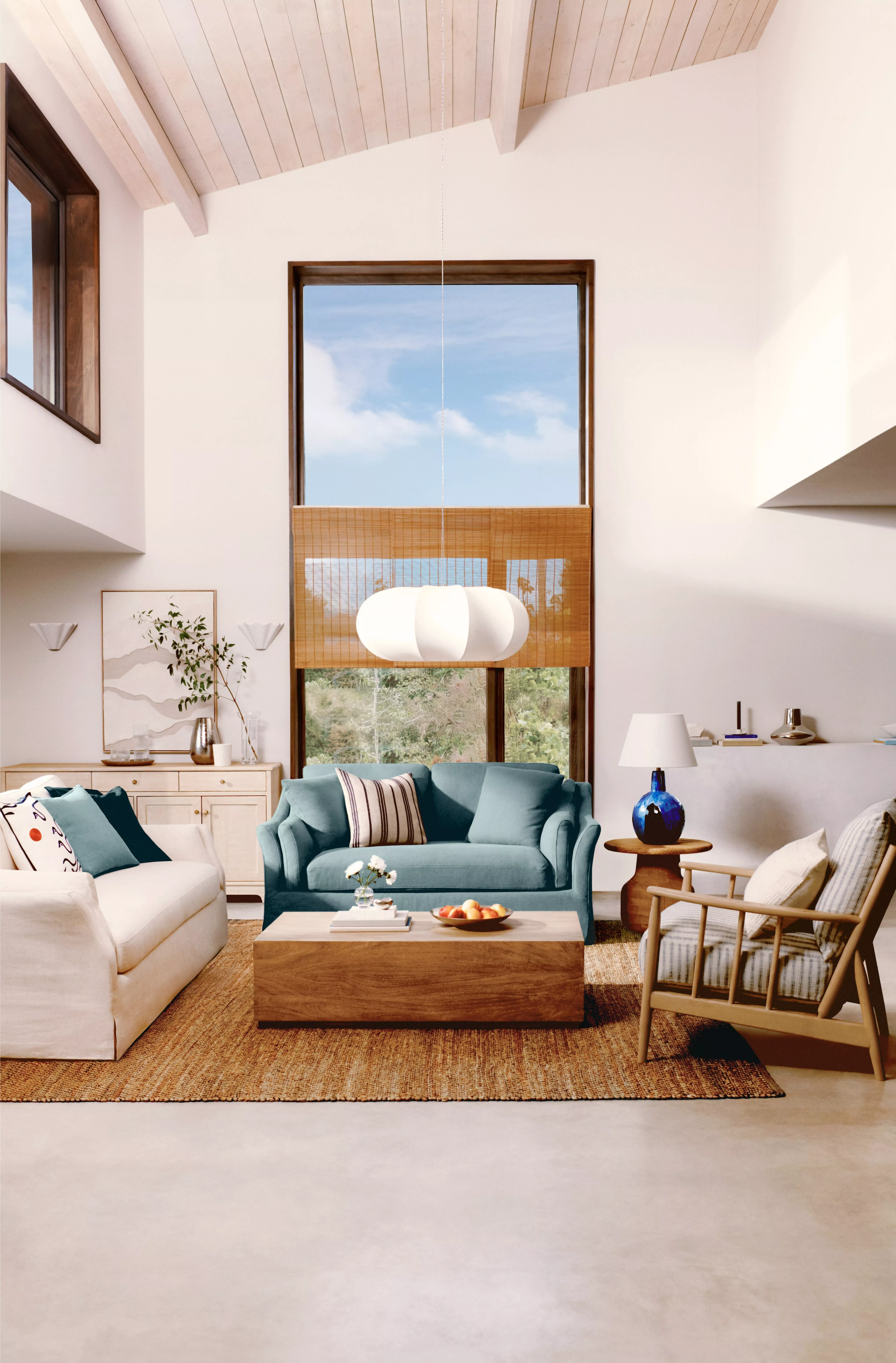 Bright living room with high ceilings, a large window, cosy sofas, wooden coffee table, and stylish decor elements.