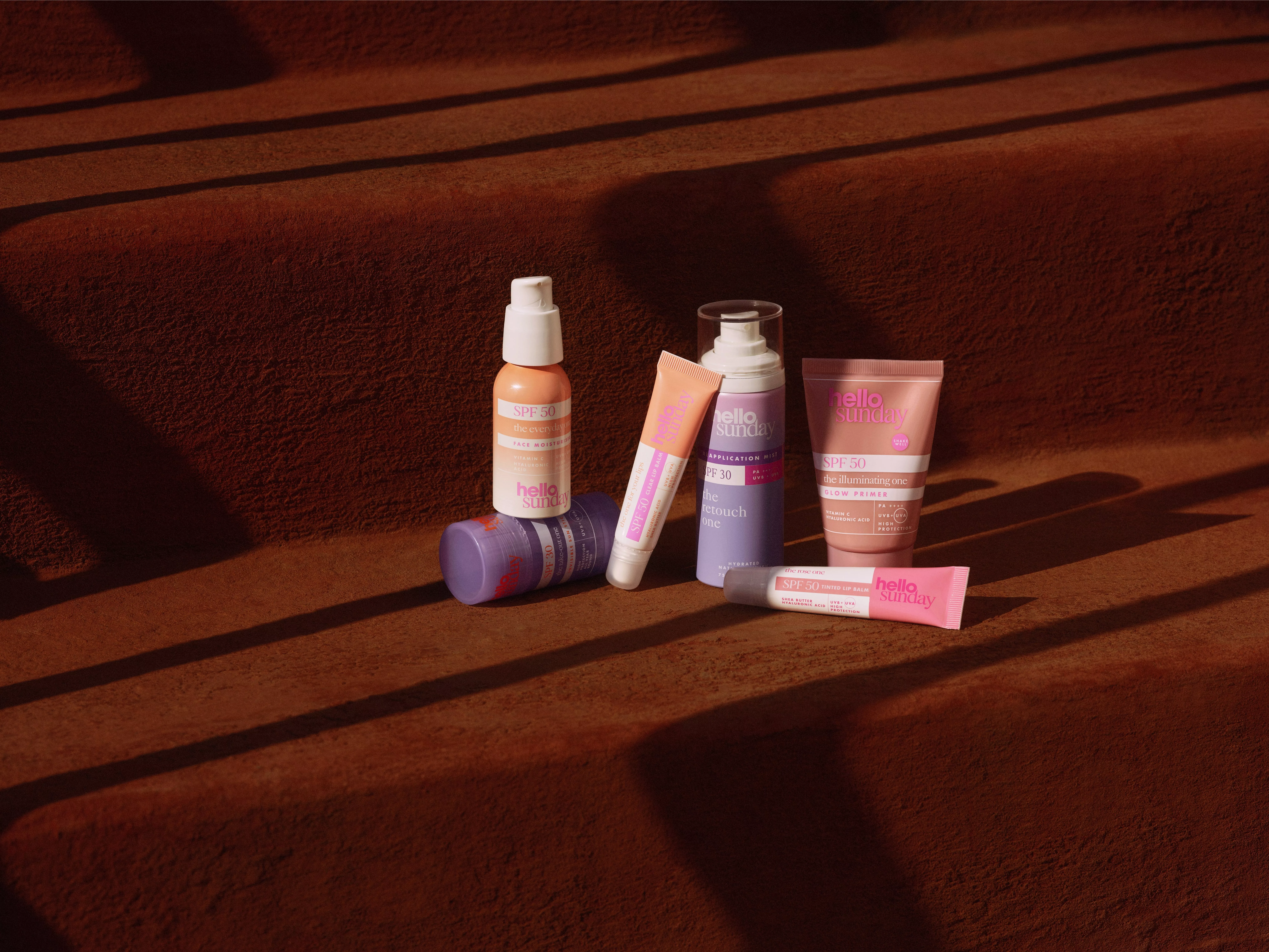 Hello Sunday SPF 50 sunscreen and glow primer skincare products arranged on sunlit terracotta steps with shadows