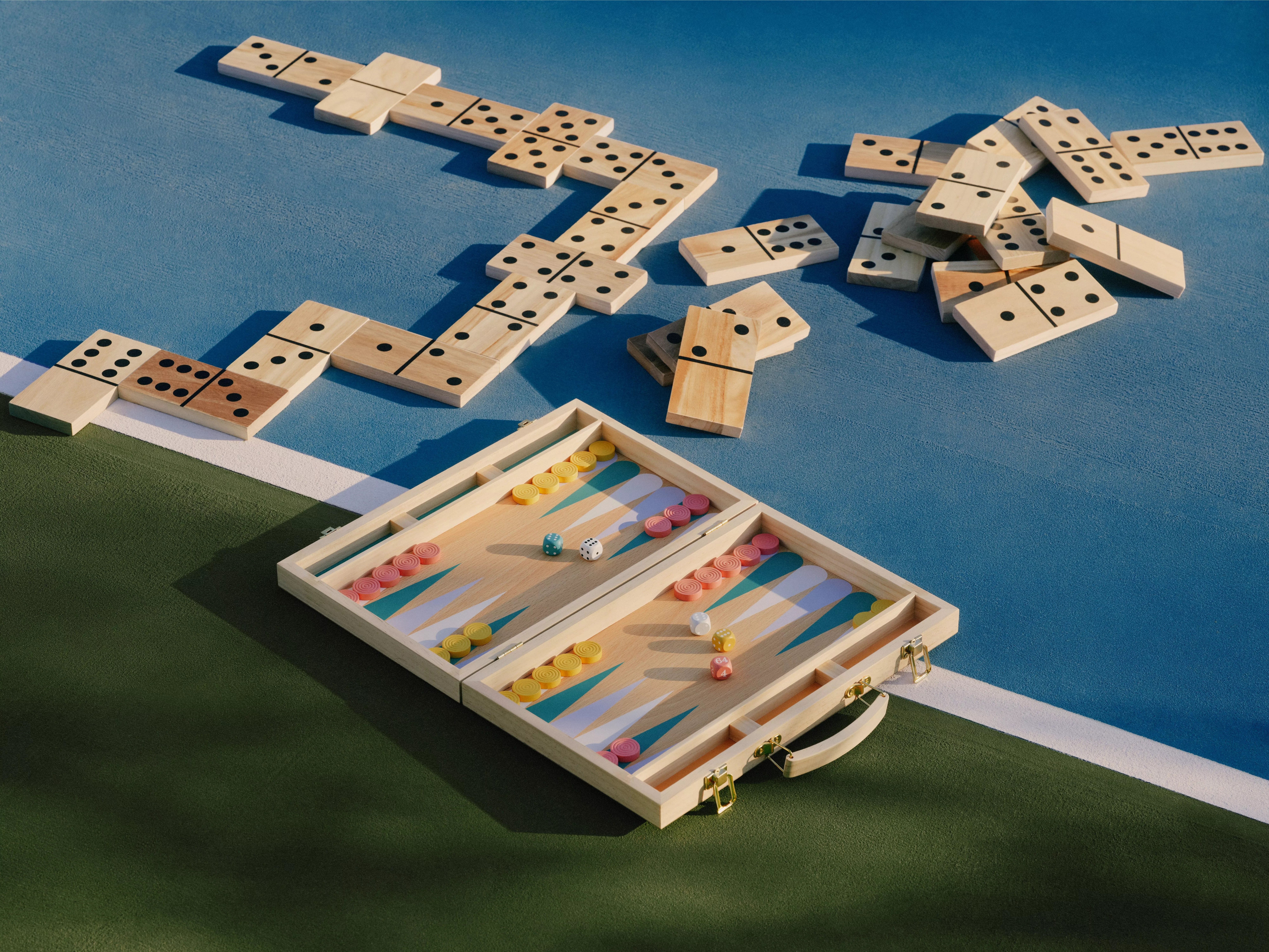 Outdoor dominoes and wooden backgammon set on a court, with dice and colourful counters in sunlight