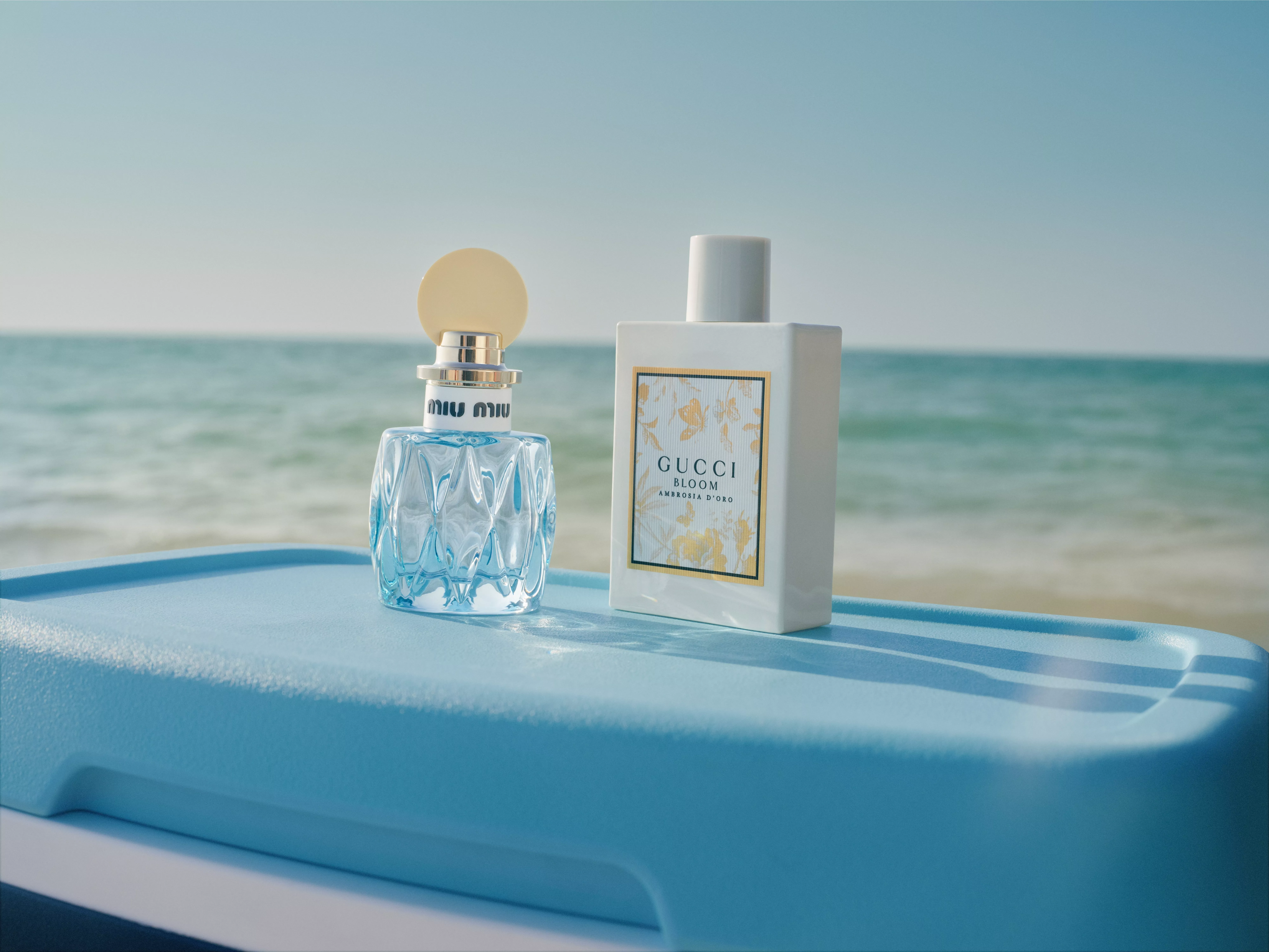 Miu Miu perfume bottle and Gucci Bloom Ambrosia d’Oro fragrance on blue cooler by the sea, summer beauty shot