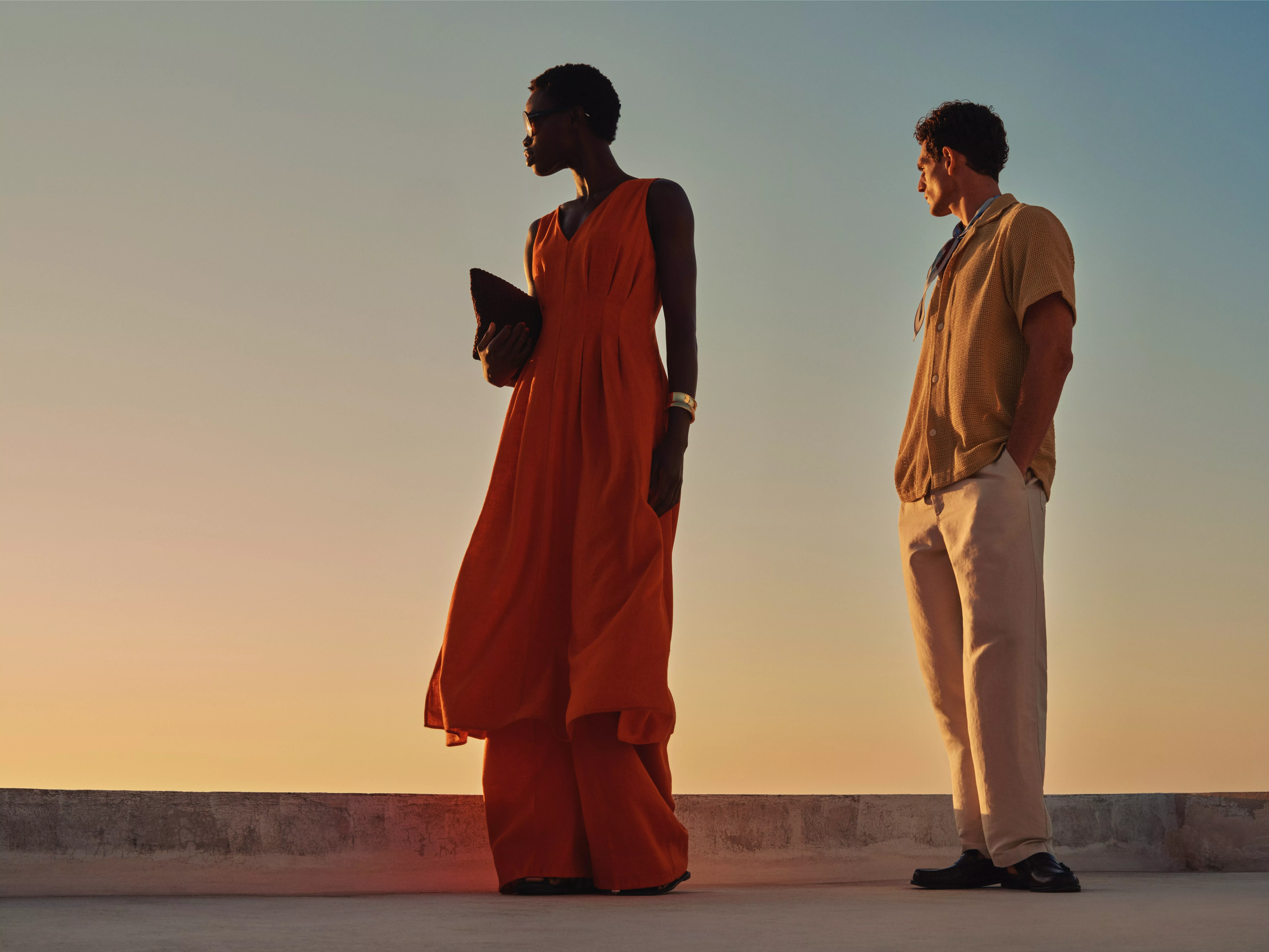 Woman in blue bikini holding a brown beach bag at sunset, fashion swimwear portrait against clear sky