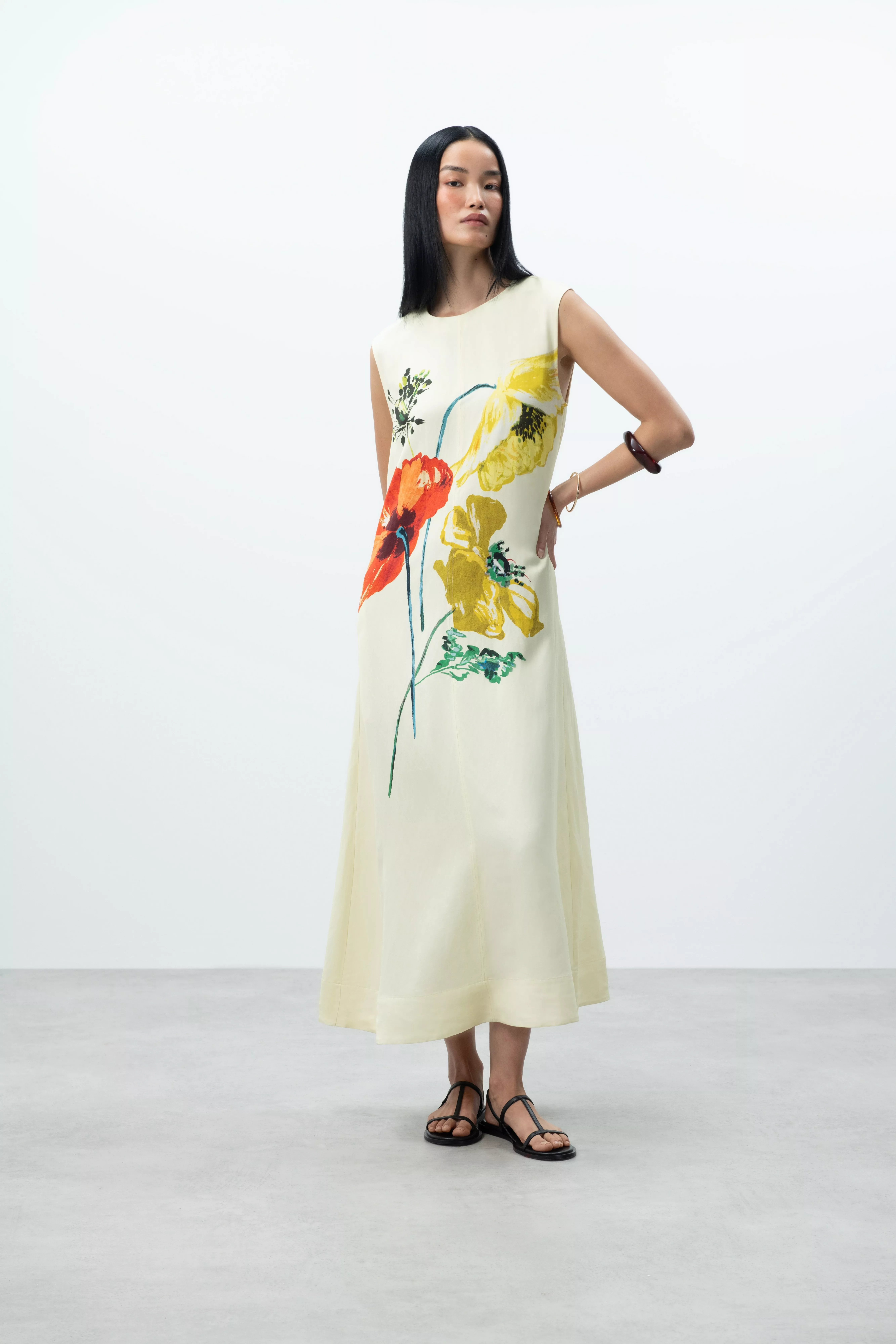 Model wearing a cream sleeveless midi dress with bold floral print, styled with black sandals in studio shot