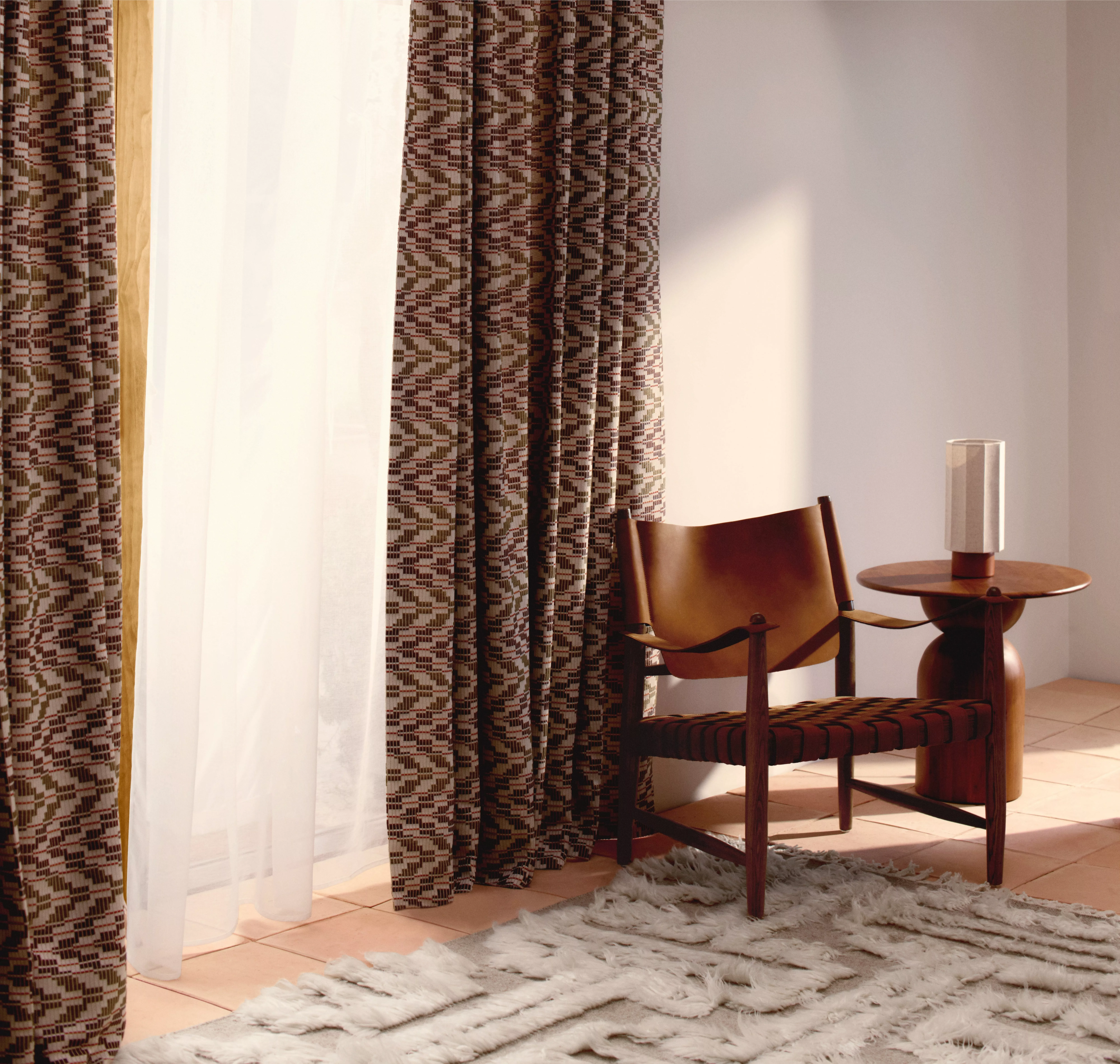 Sunlit room with patterned curtains, leather chair, wooden table and textured rug. Warm, inviting decor style.