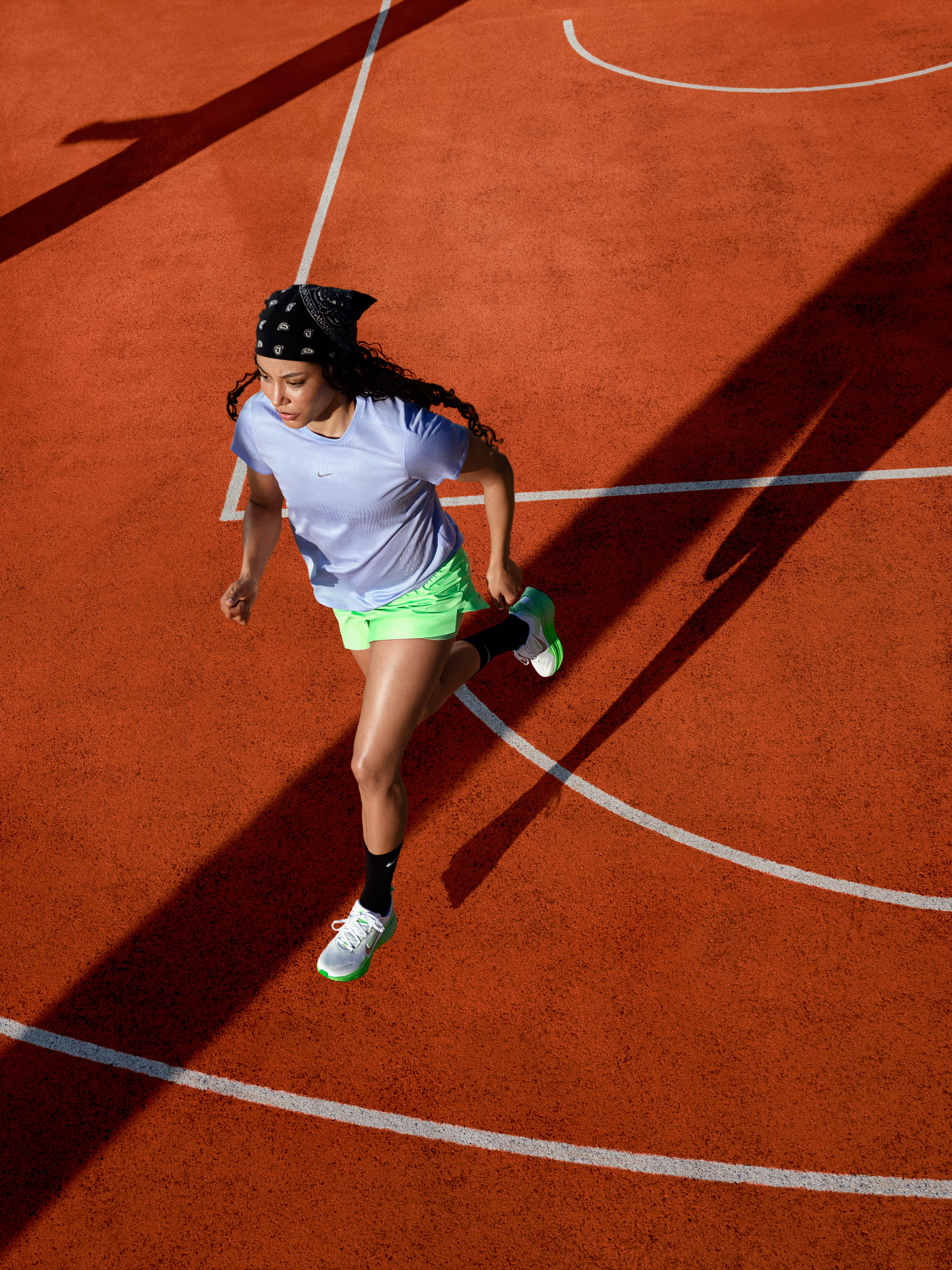 Female athlete sprinting on an outdoor athletics track, wearing a white top, neon shorts and running shoes