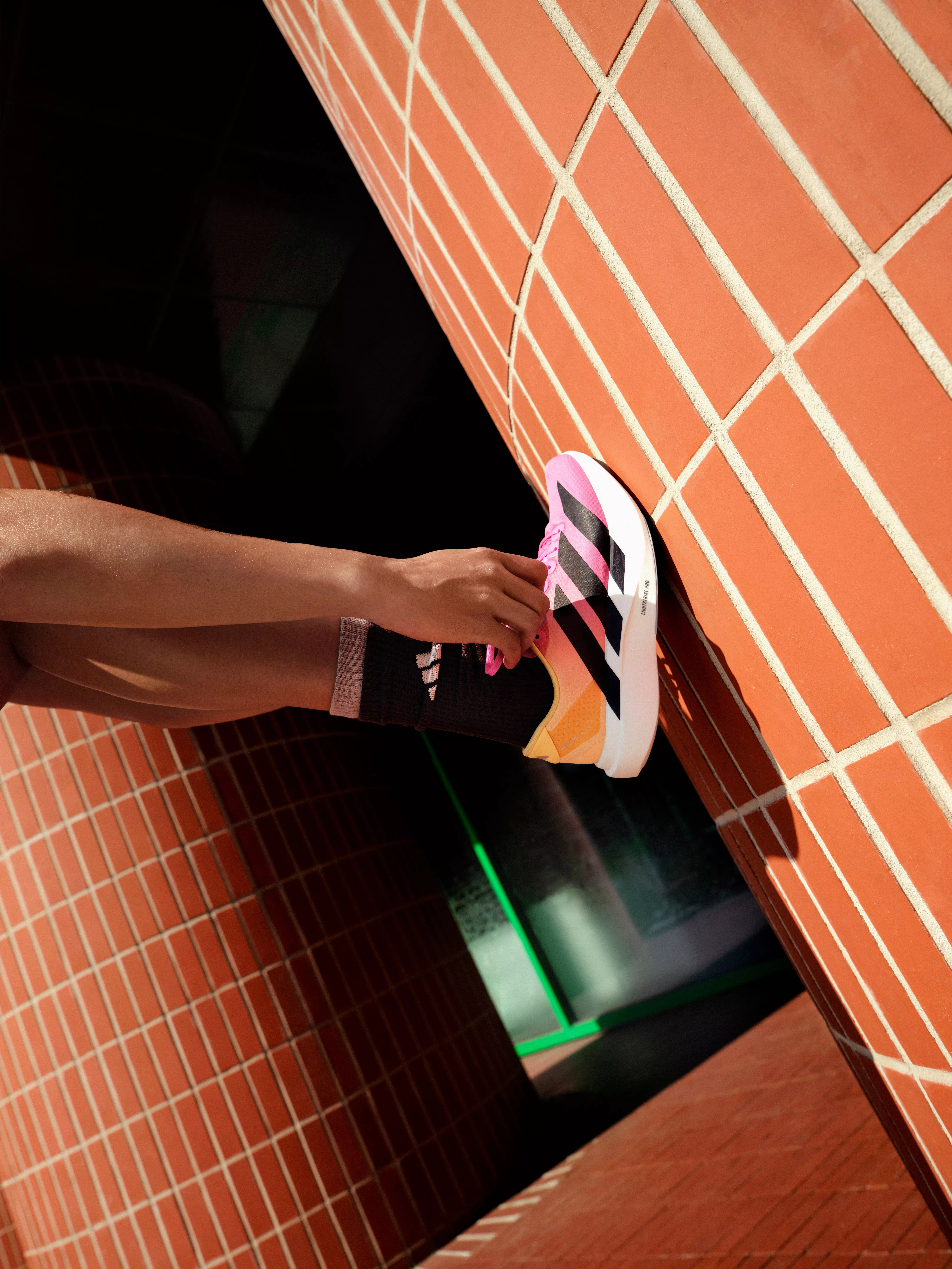Close-up of runner tying pink-laced trainers beside orange tiled wall in urban corridor, sports footwear detail