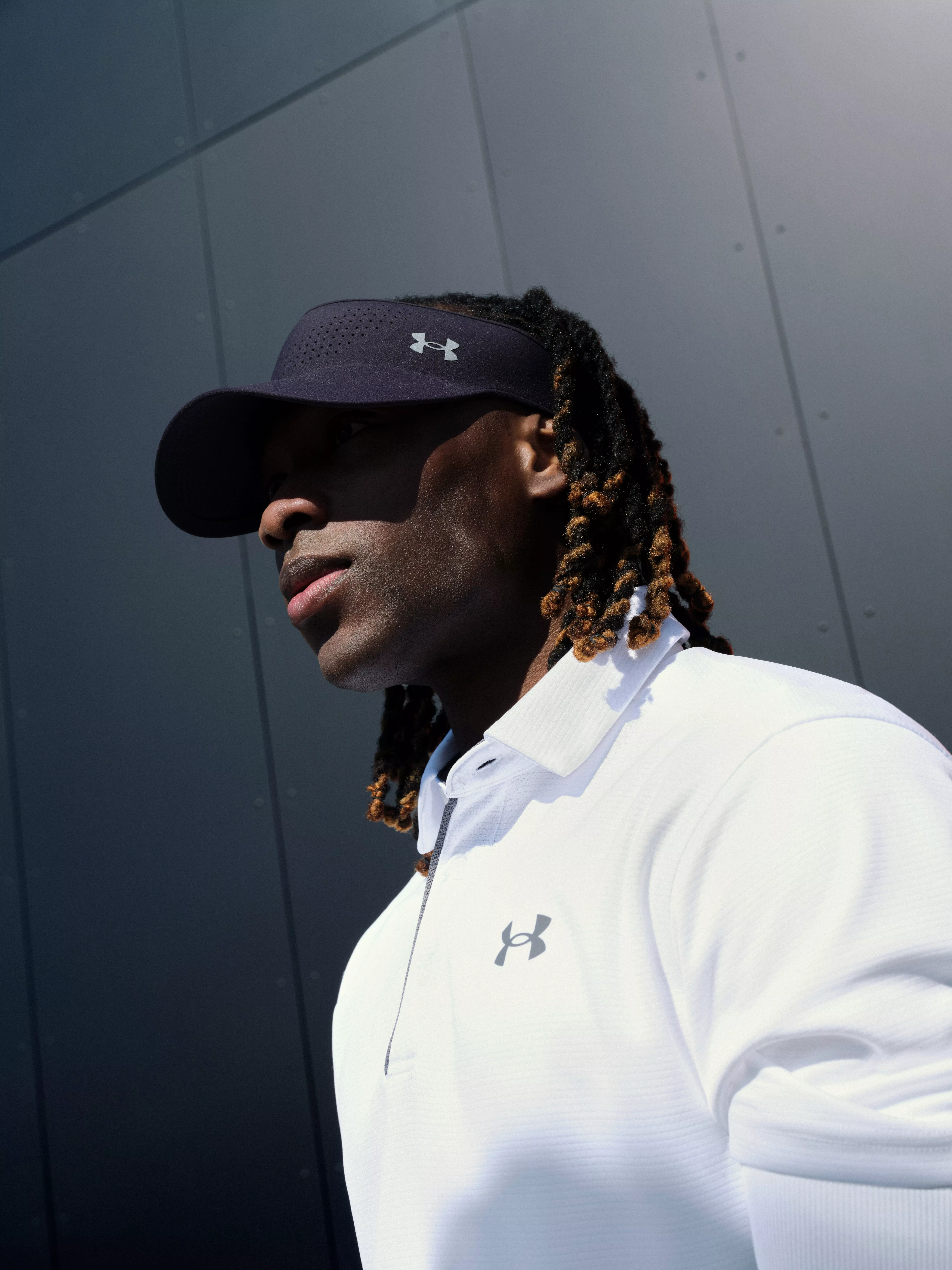 Side profile of athlete in Under Armour visor and white polo shirt, outdoor sportswear portrait in shade