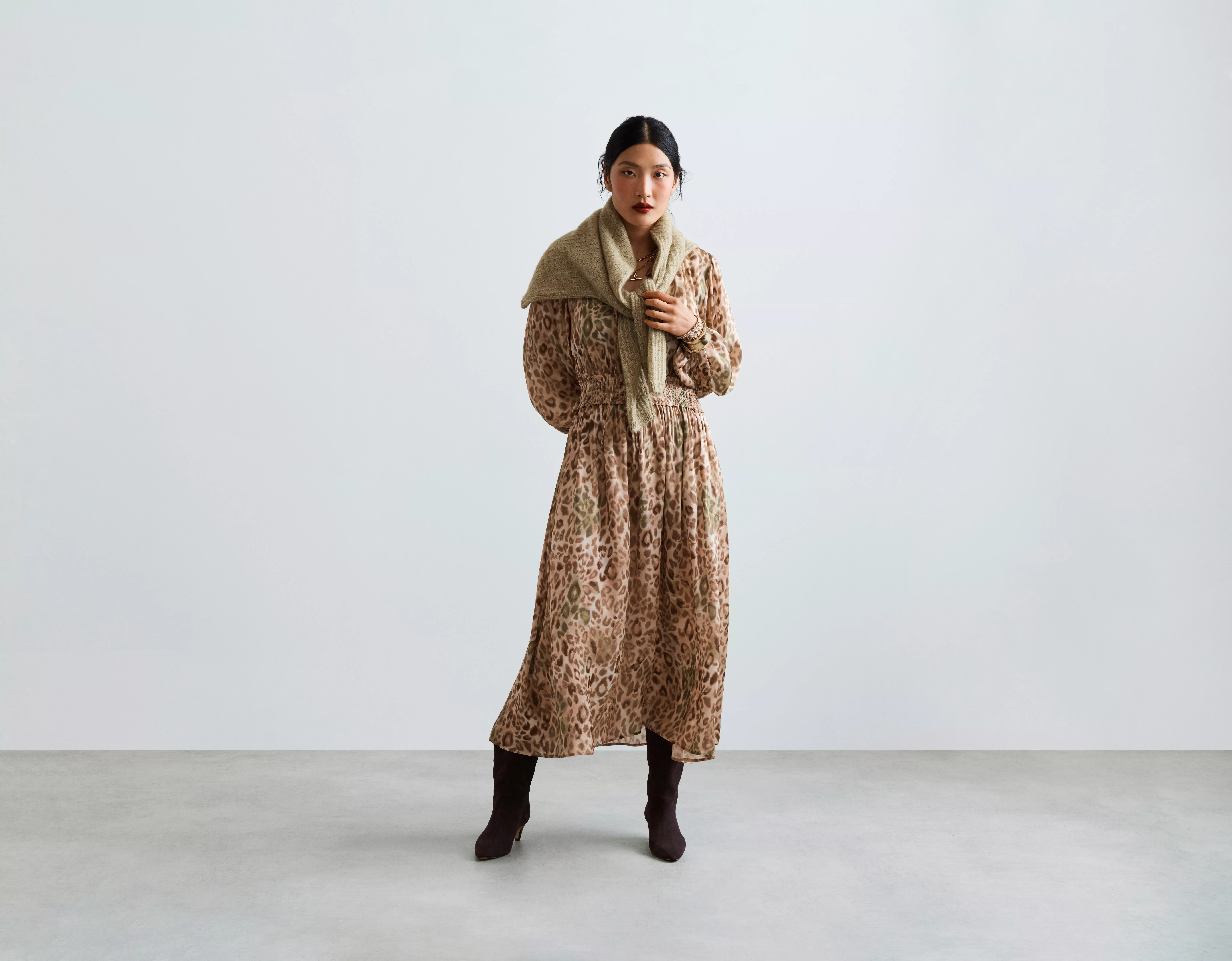 Fashion model in leopard print midi dress with beige scarf and black boots, studio portrait on grey backdrop