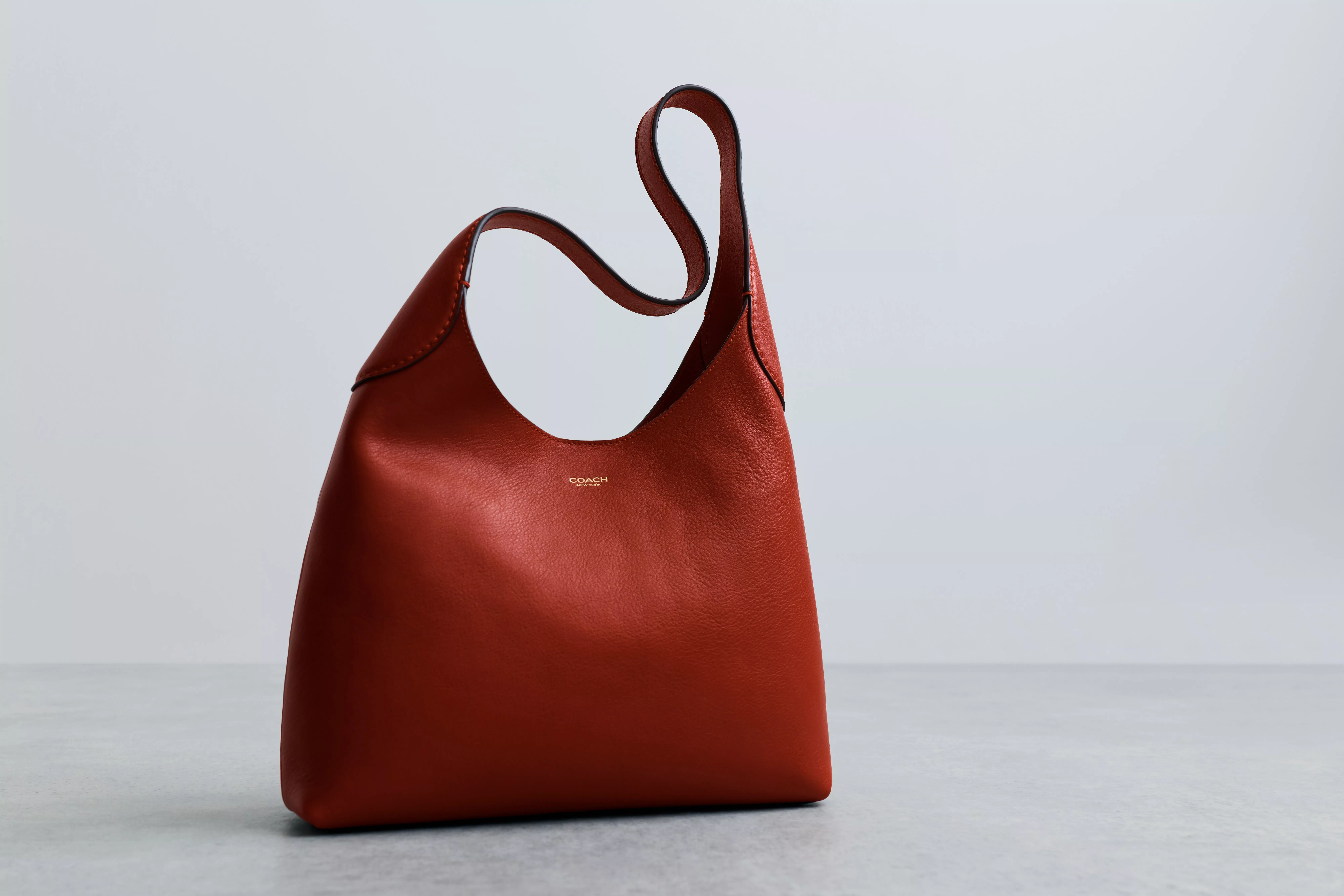 Red leather Coach hobo shoulder bag with curved strap, minimalist studio product photo on light grey background