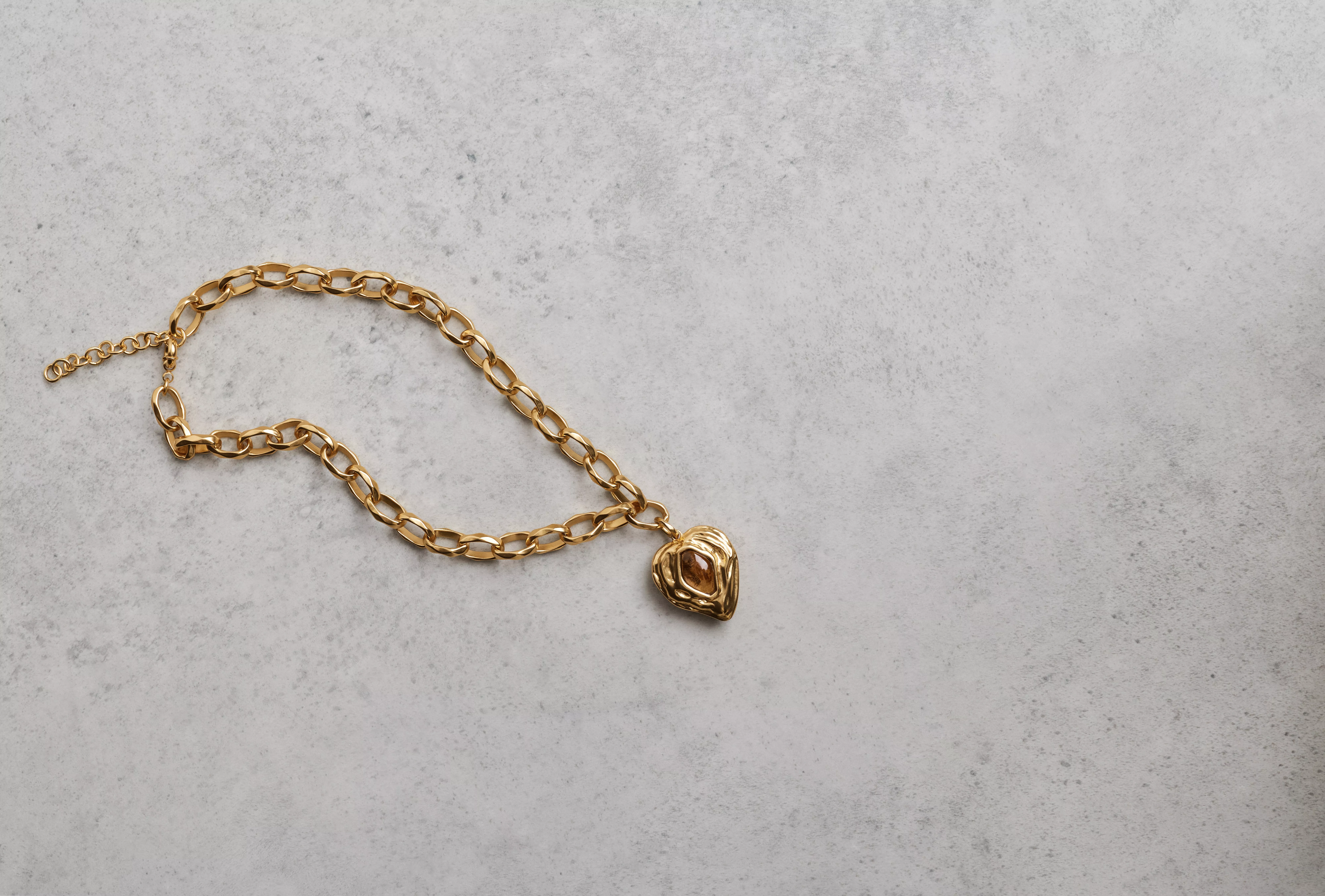 Gold chain necklace with heart pendant charm on grey stone background, minimalist jewellery flat lay photo