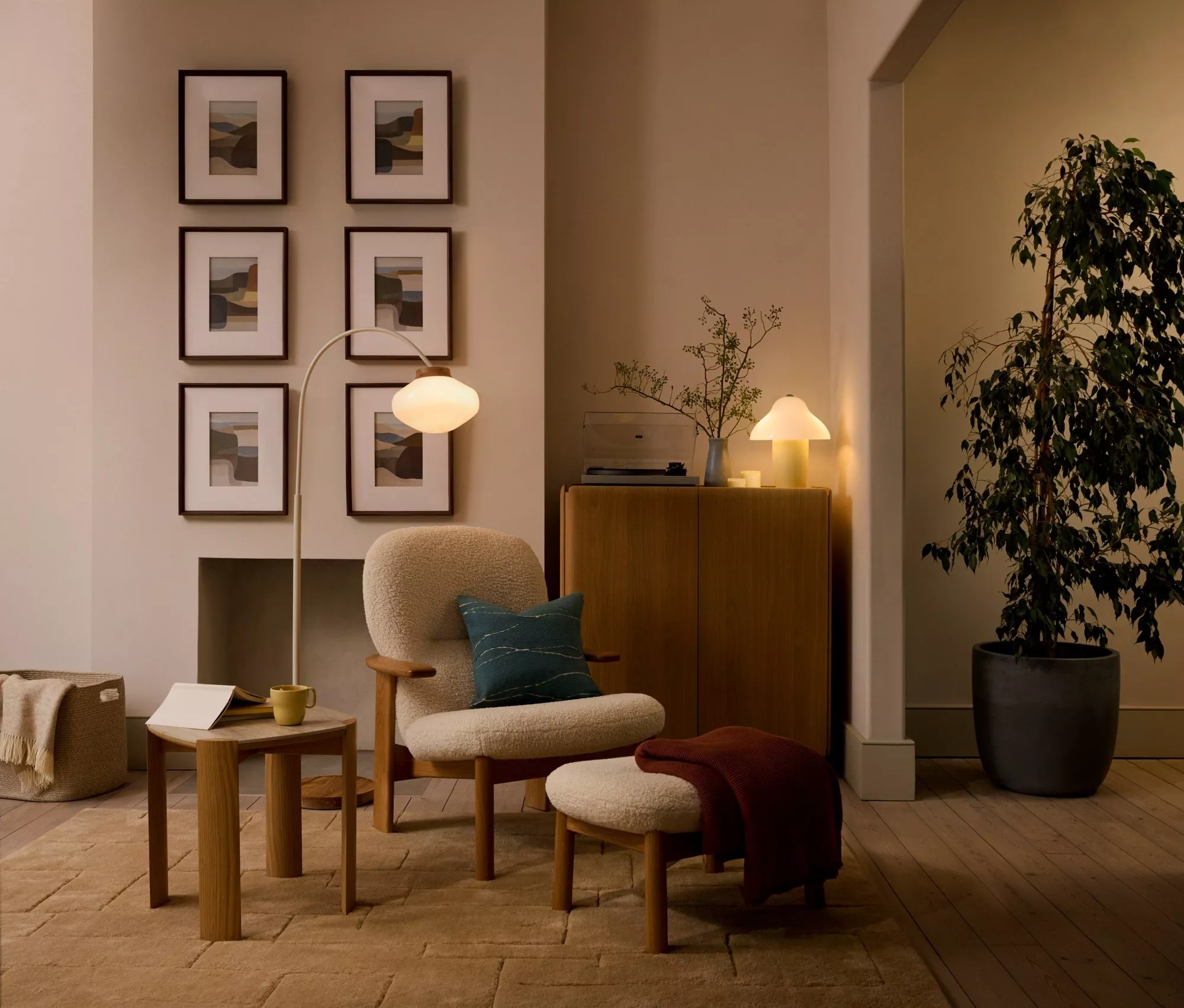 Cosy modern living room with armchair, floor lamp, framed art wall, sideboard, houseplant and wooden flooring