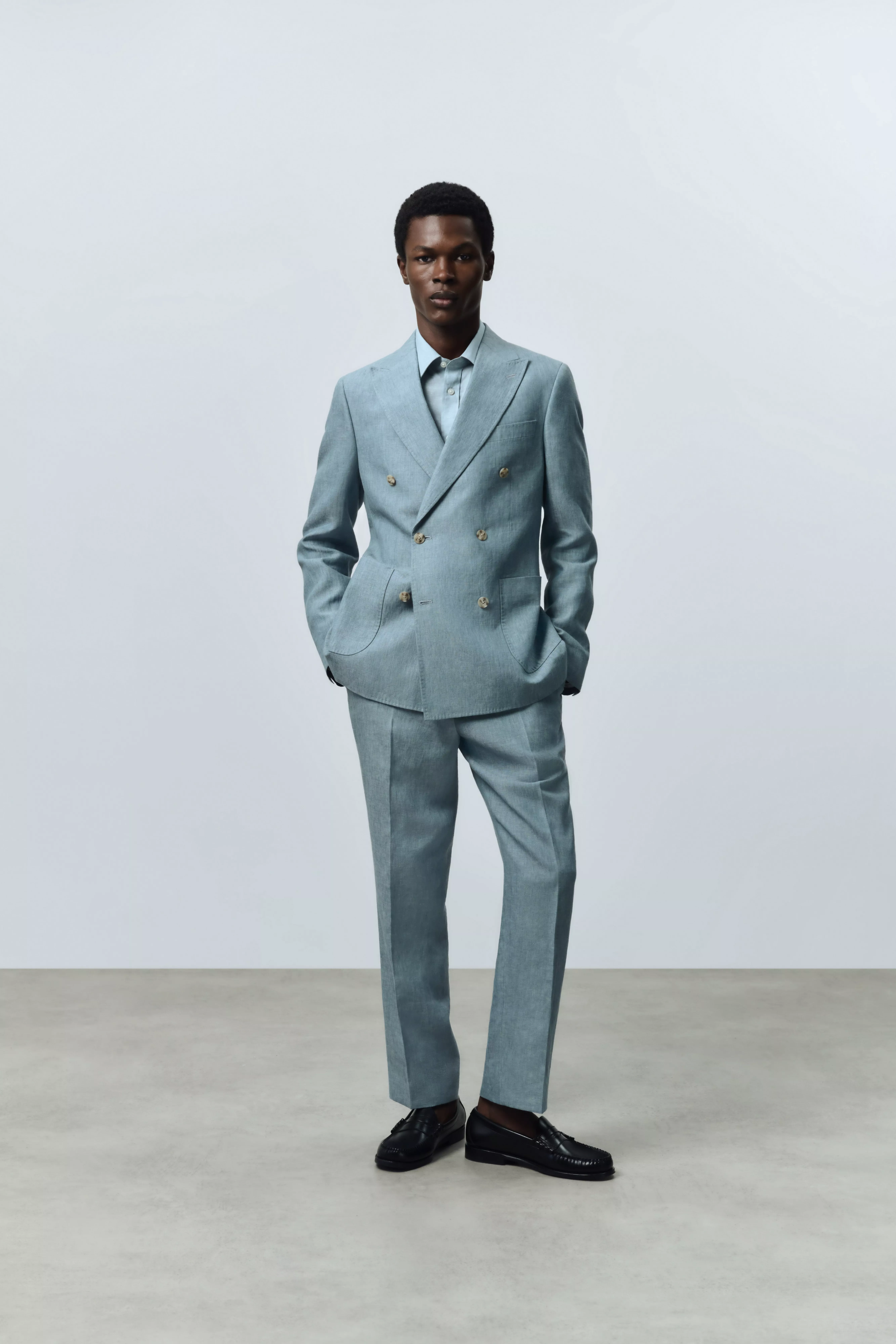 Full-length studio photo of man in light blue double-breasted suit with black loafers on grey backdrop