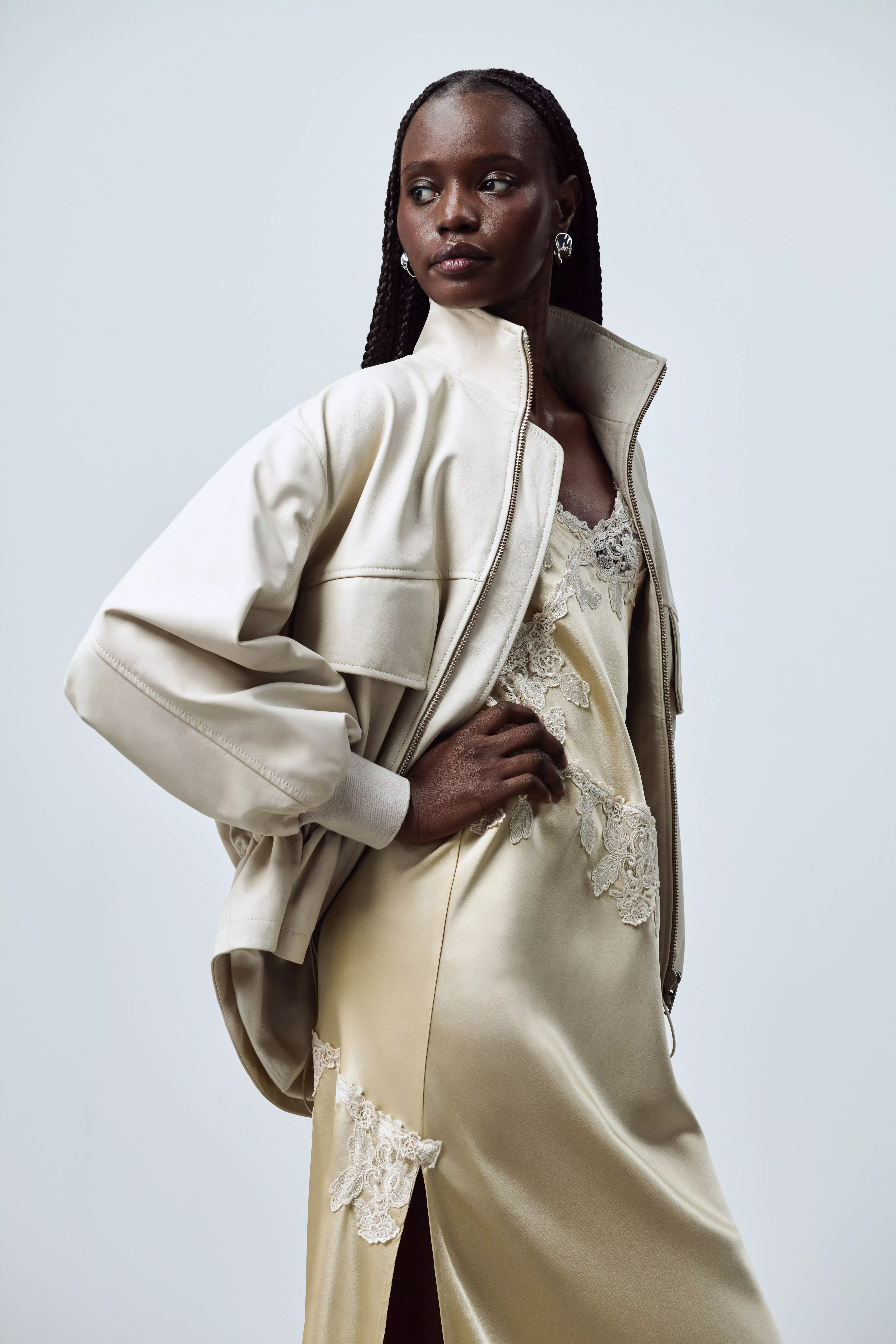 A woman in a brown one-shoulder top and dark jeans, holding a black purse and wearing black heels.