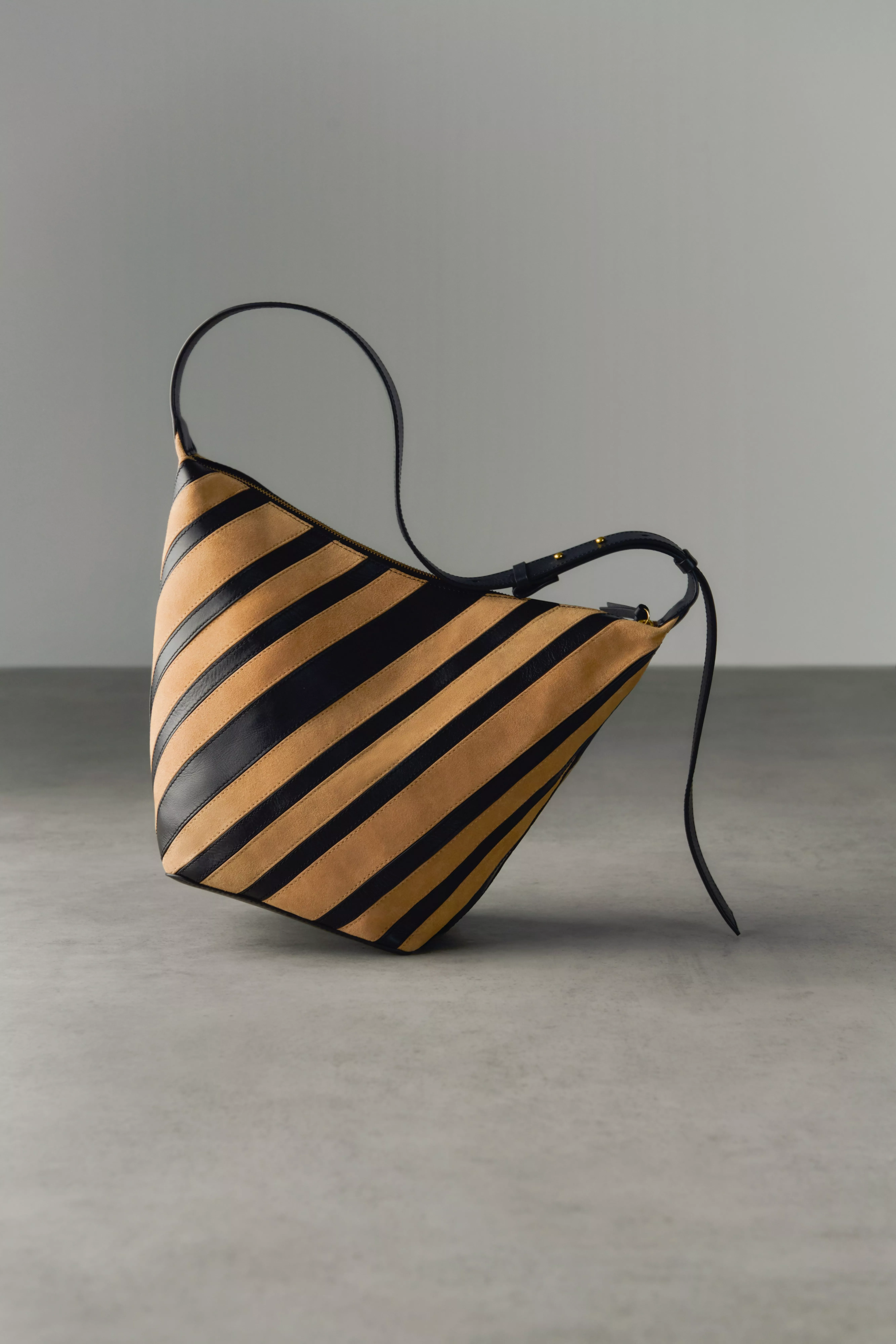 Tan and black striped leather shoulder bag with adjustable strap, minimalist fashion accessory on grey studio background