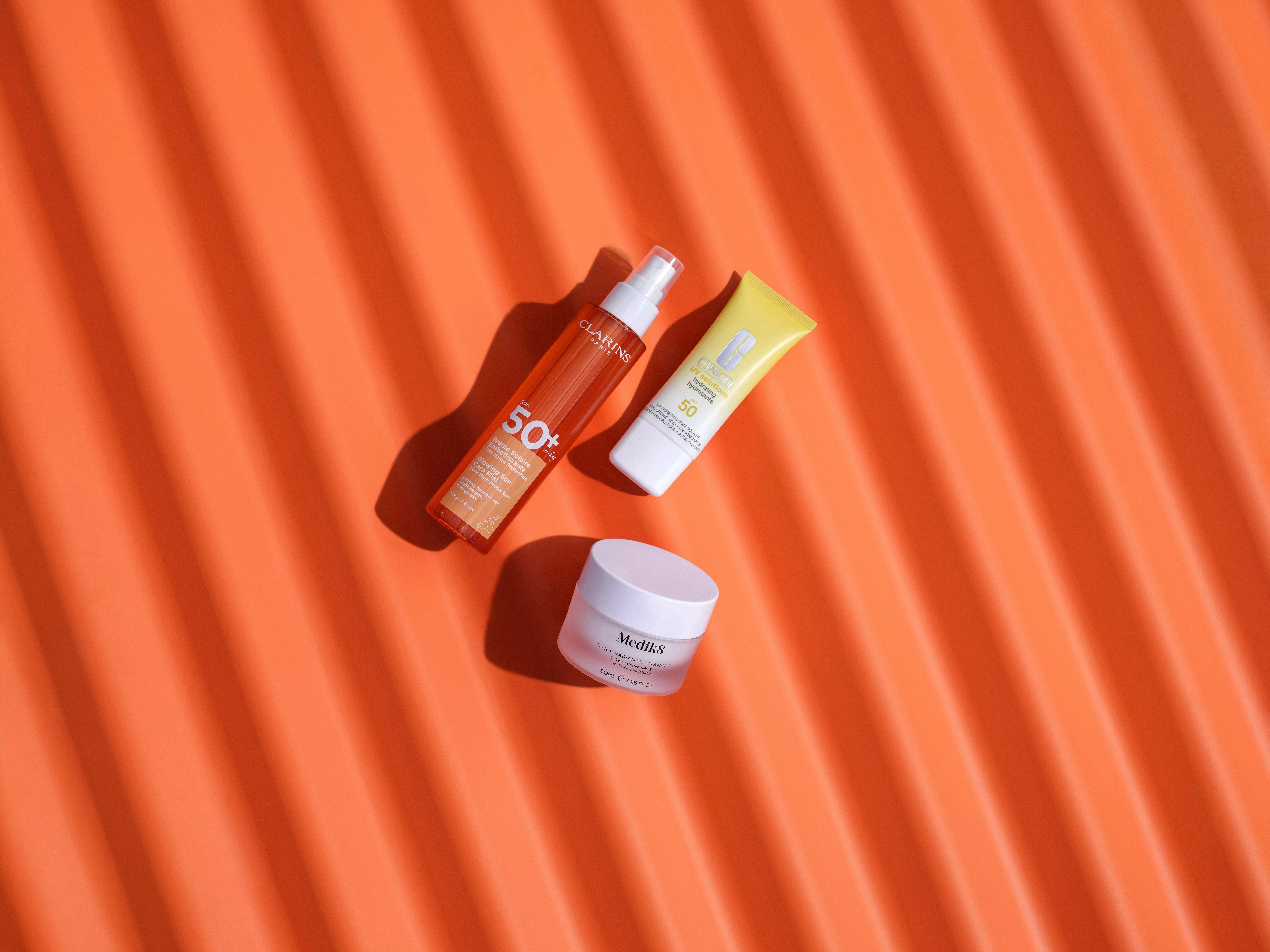Sun care skincare flat lay with SPF 50 spray, sunscreen tube and moisturiser jar on orange background