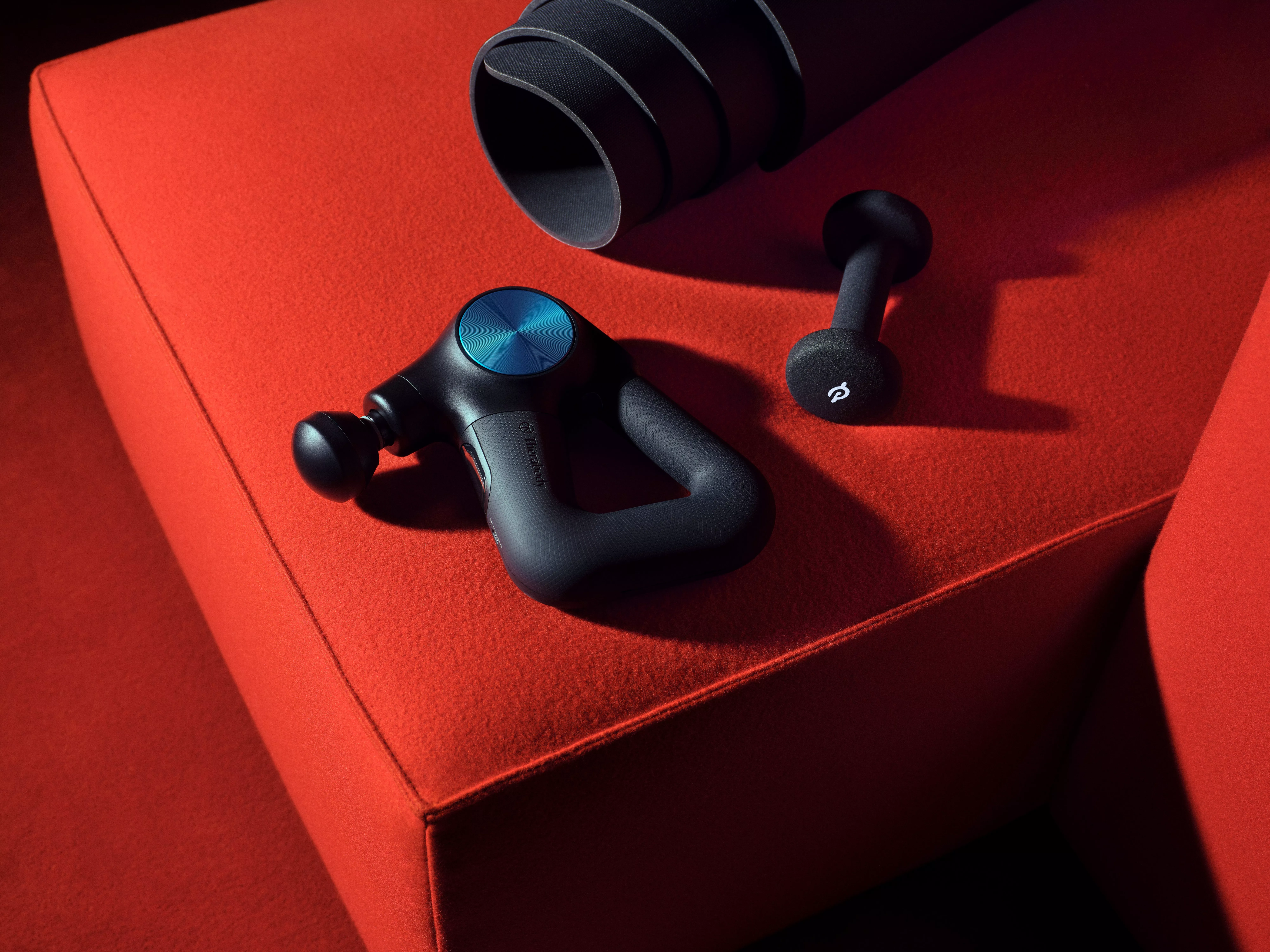 Black handheld percussion massage gun with attachments on red sofa, fitness recovery and muscle relief device