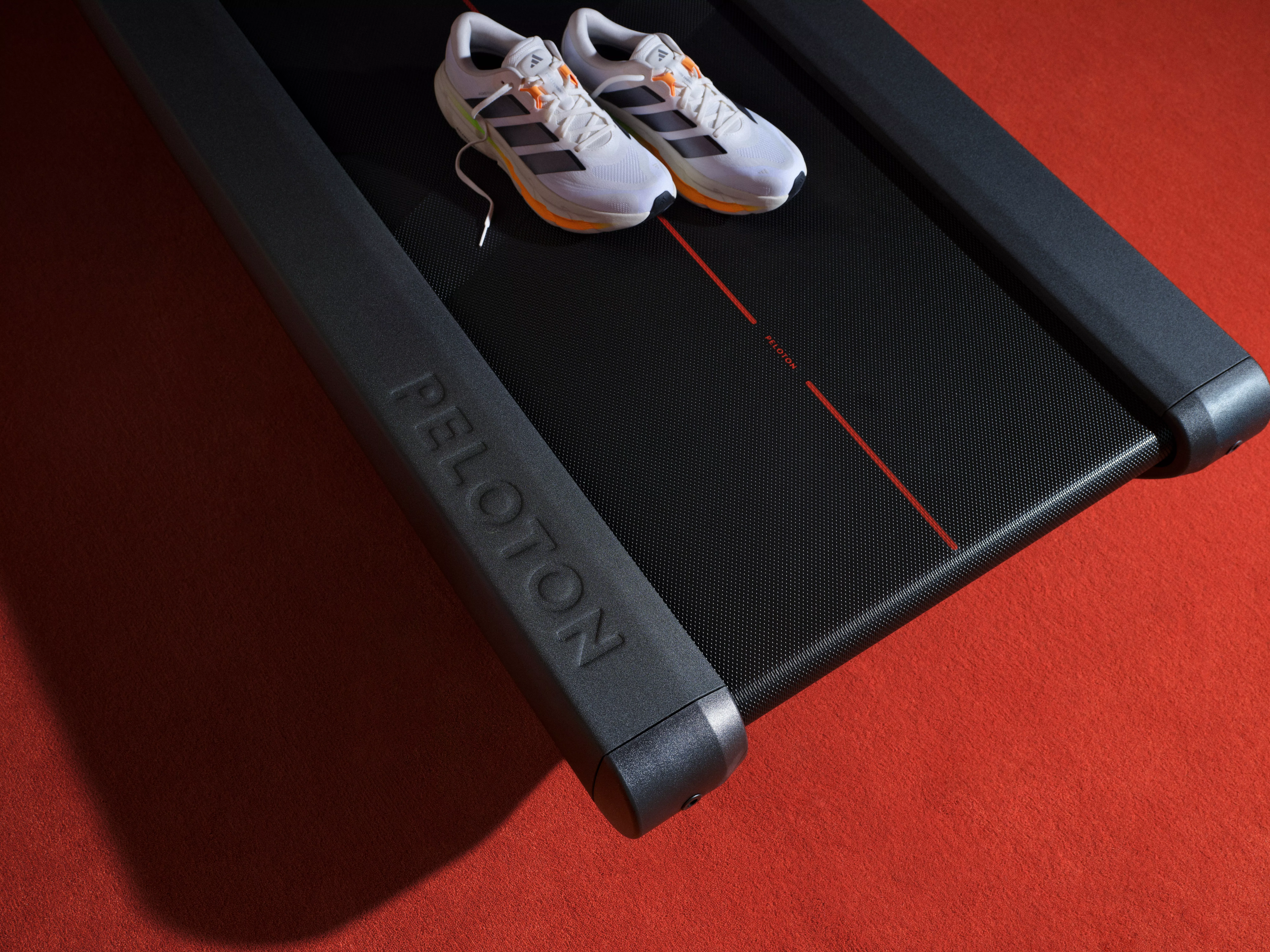 White running trainers on a Peloton treadmill belt in a gym, fitness equipment close-up on red track surface