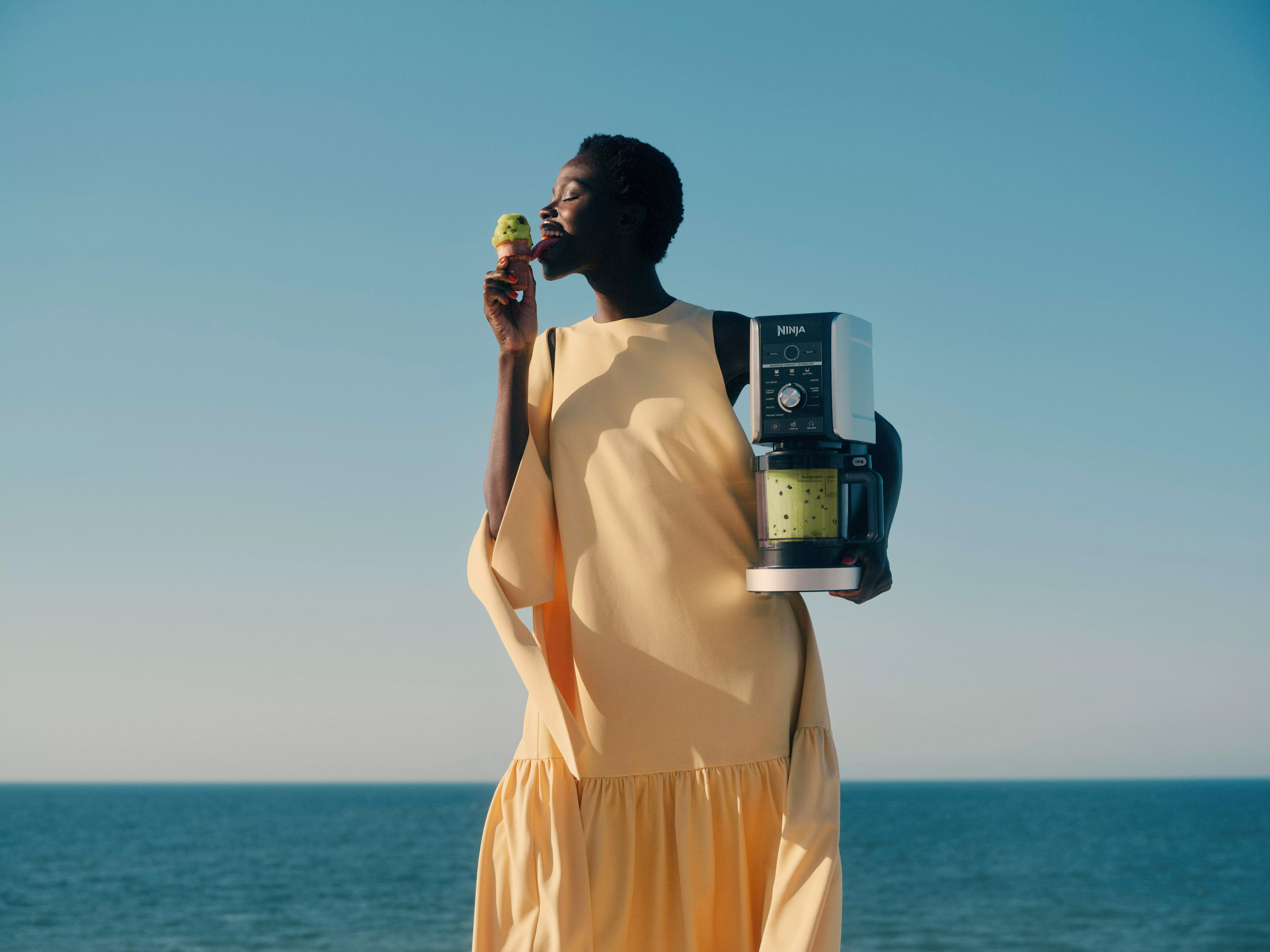 Woman by the sea holding Ninja ice cream maker and tasting pistachio gelato on a sunny summer day outdoors