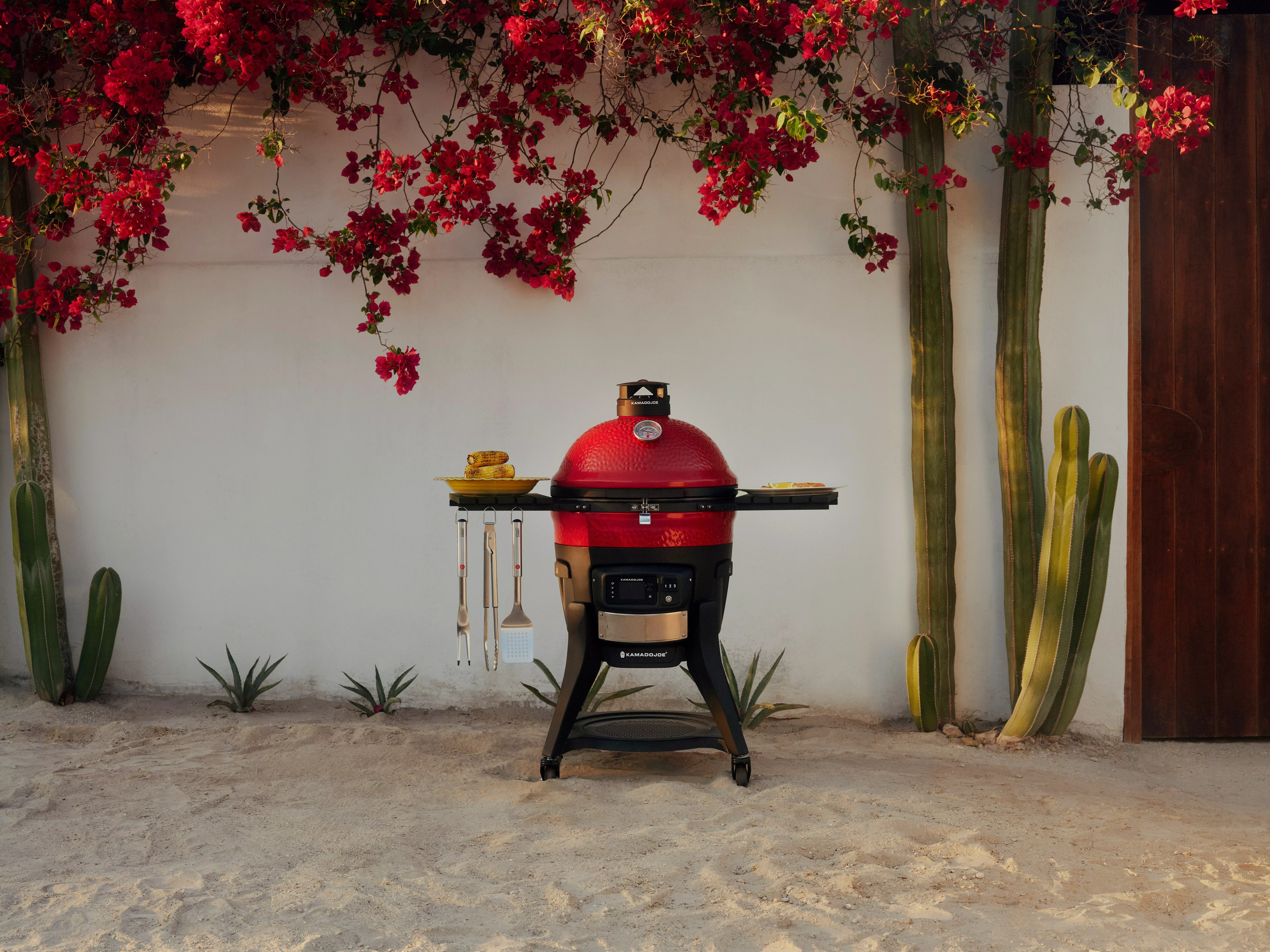 Black kettle charcoal barbecue grill on wheeled stand, photographed on a white plinth against dark asphalt.