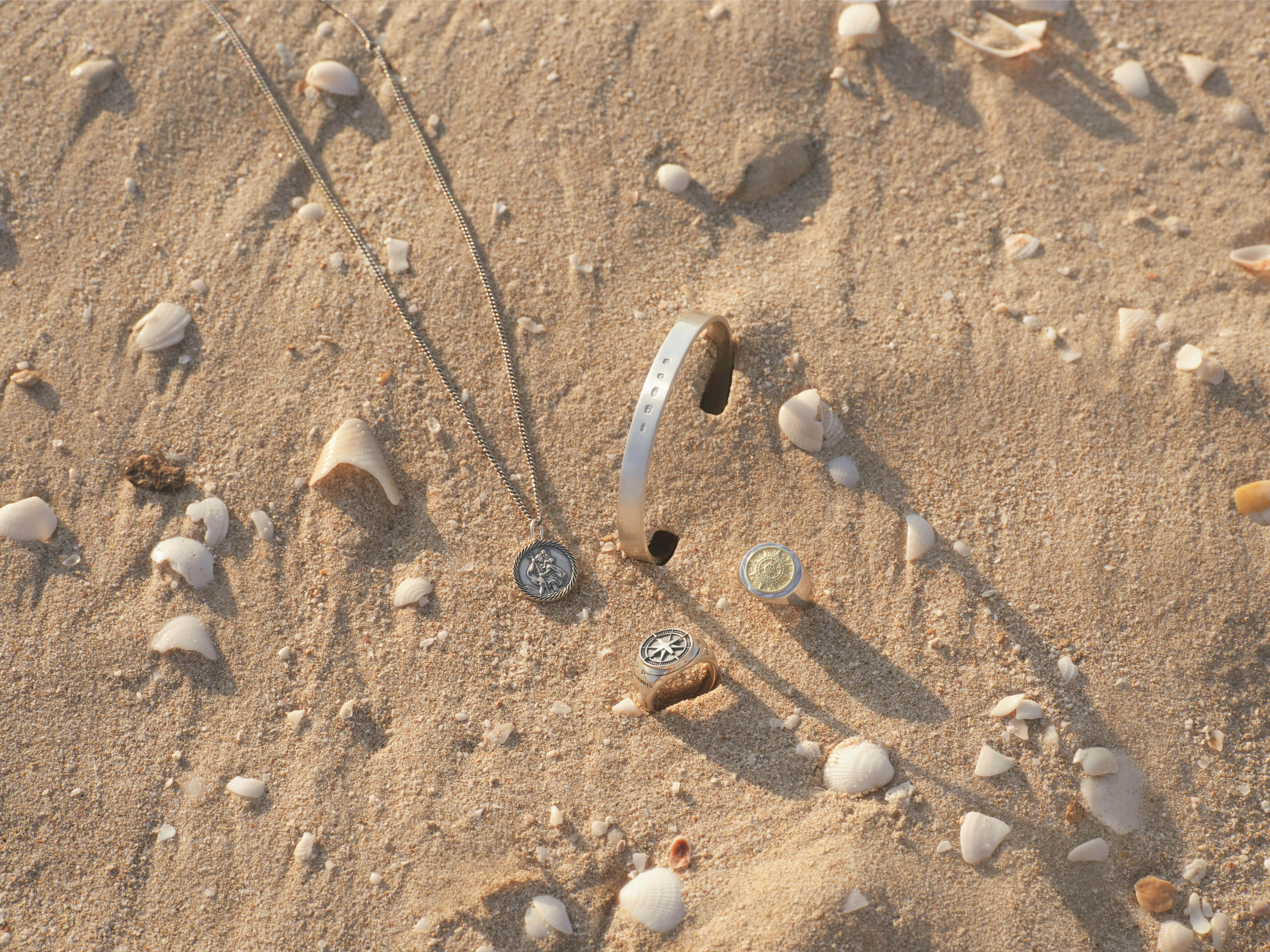 Gold chain necklace with stacked gold rings, including a rainbow gemstone band, on a neutral stone surface