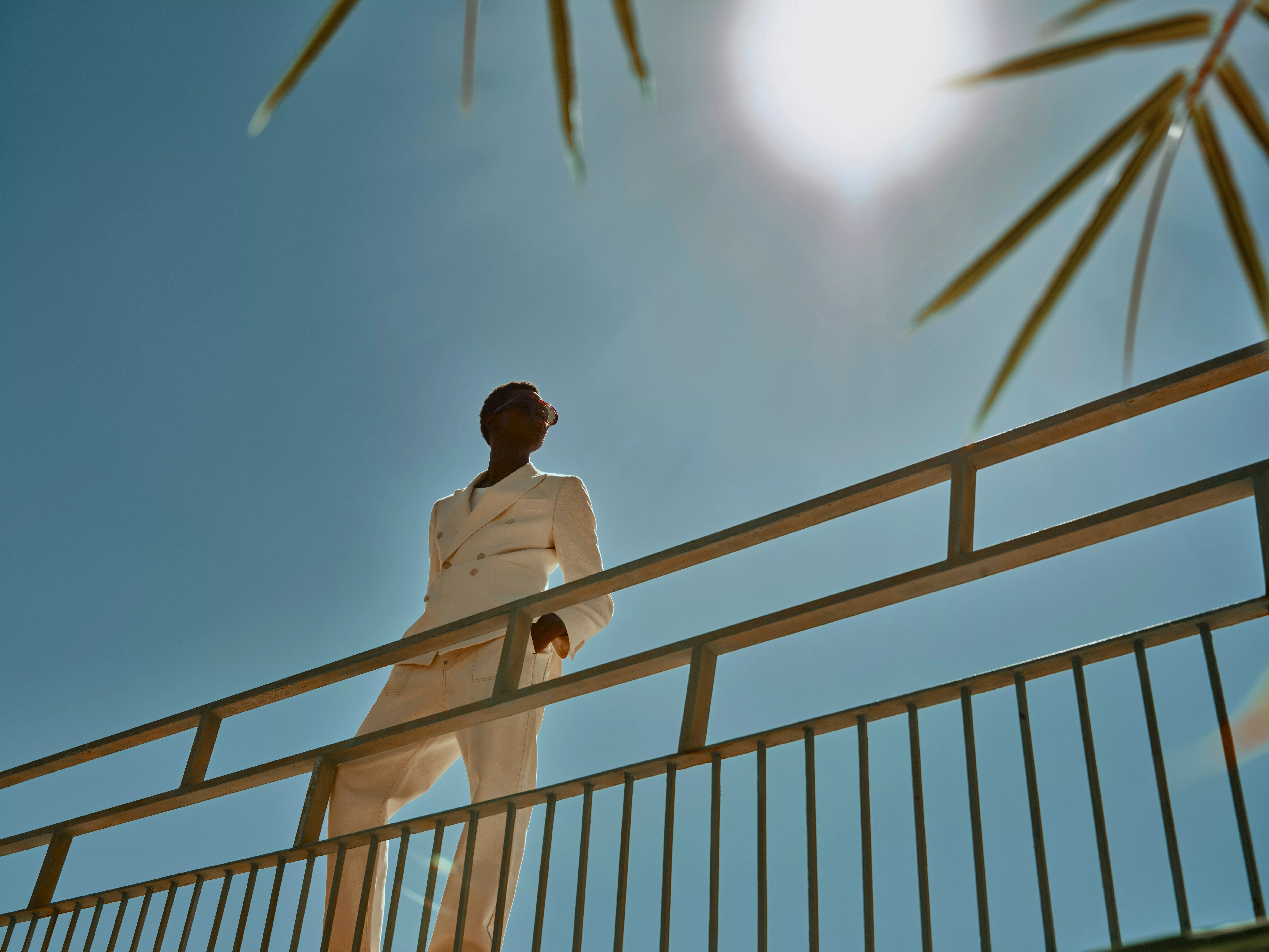 Stylish man in sunglasses lounging in a swimming pool, wearing blue shirt and patterned swim shorts in sunlight