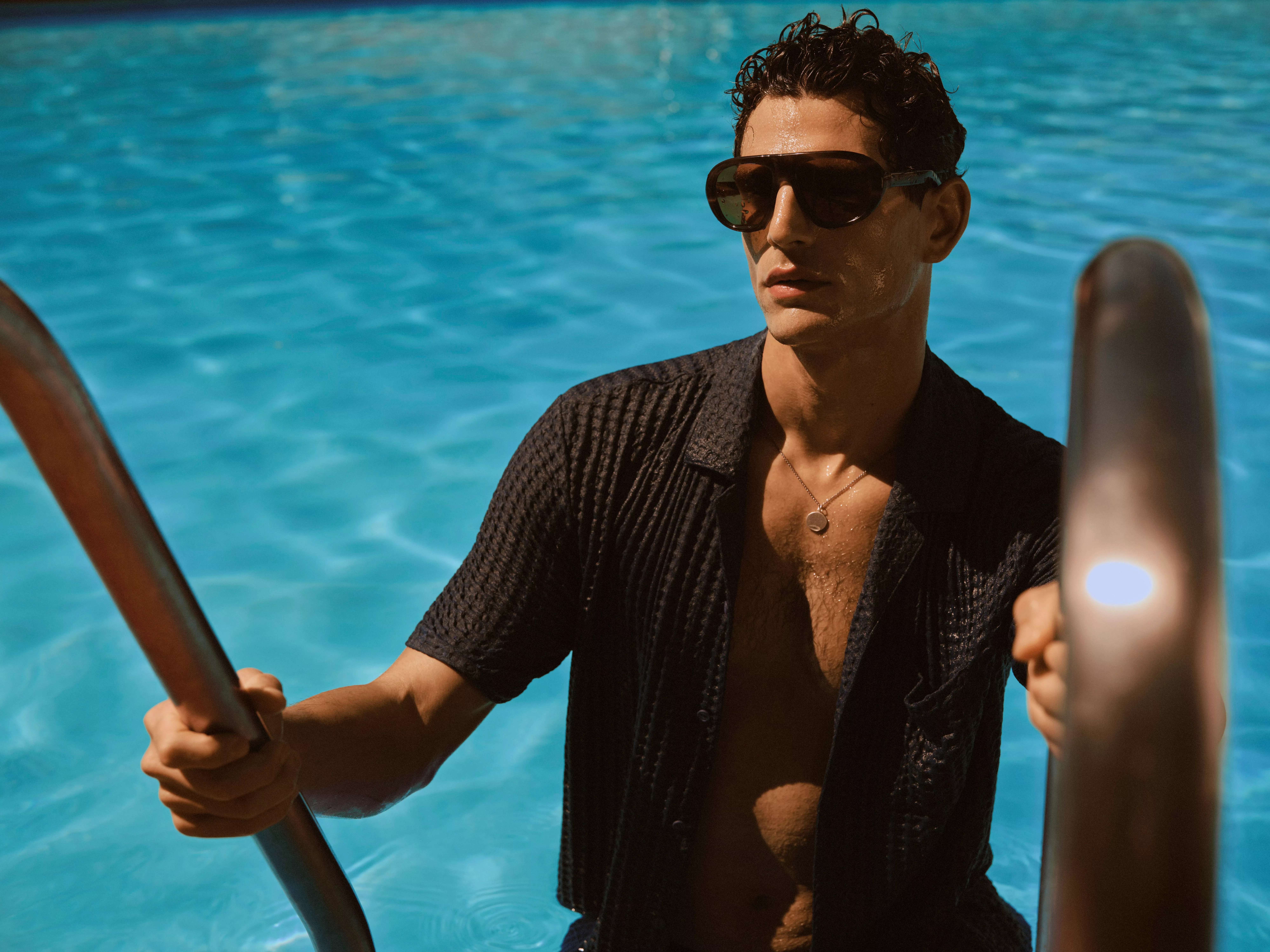 Man wearing black sunglasses stepping out of a swimming pool