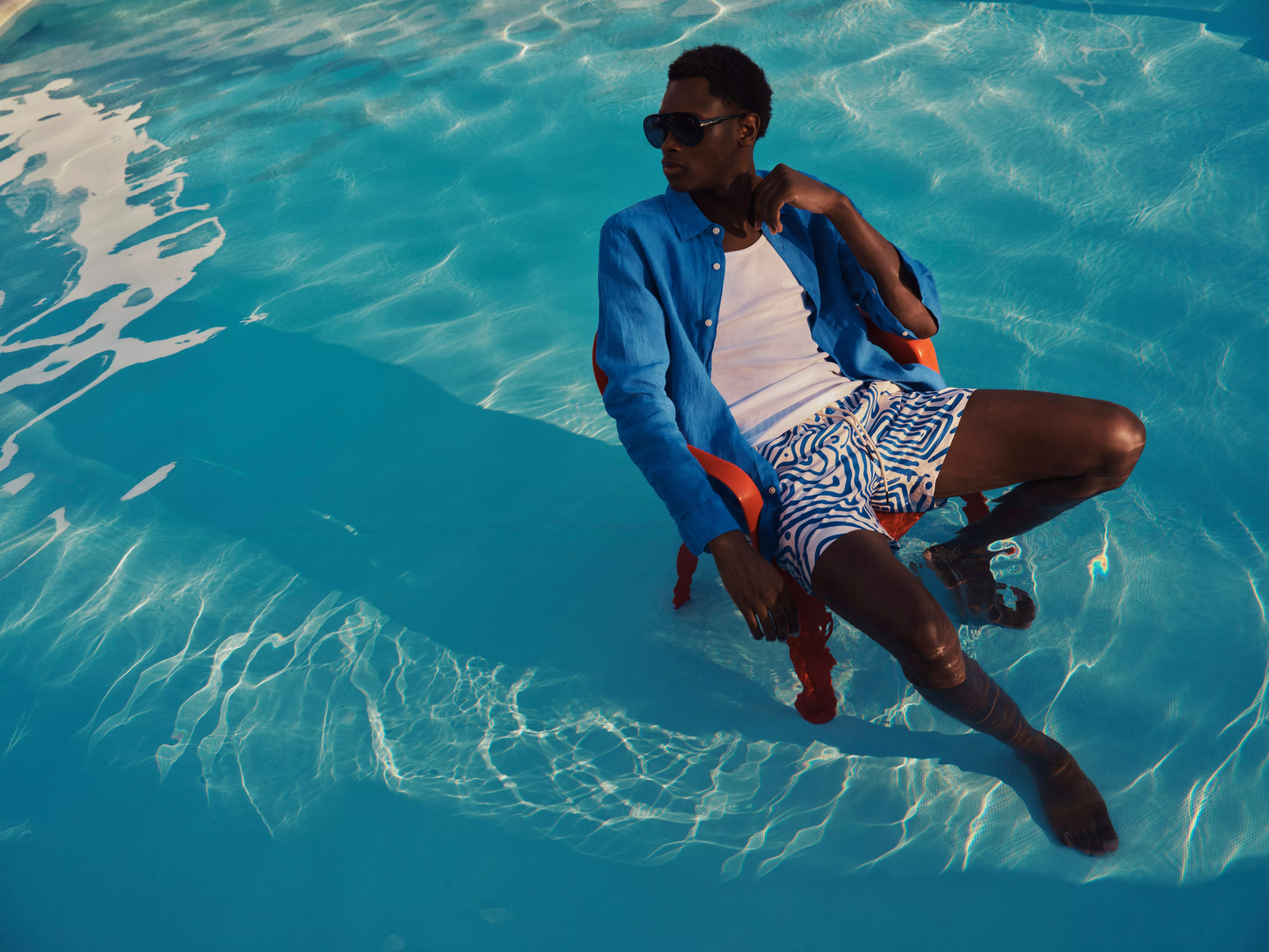 Man wearing a blue linen shirt sitting on a chair in a swimming pool