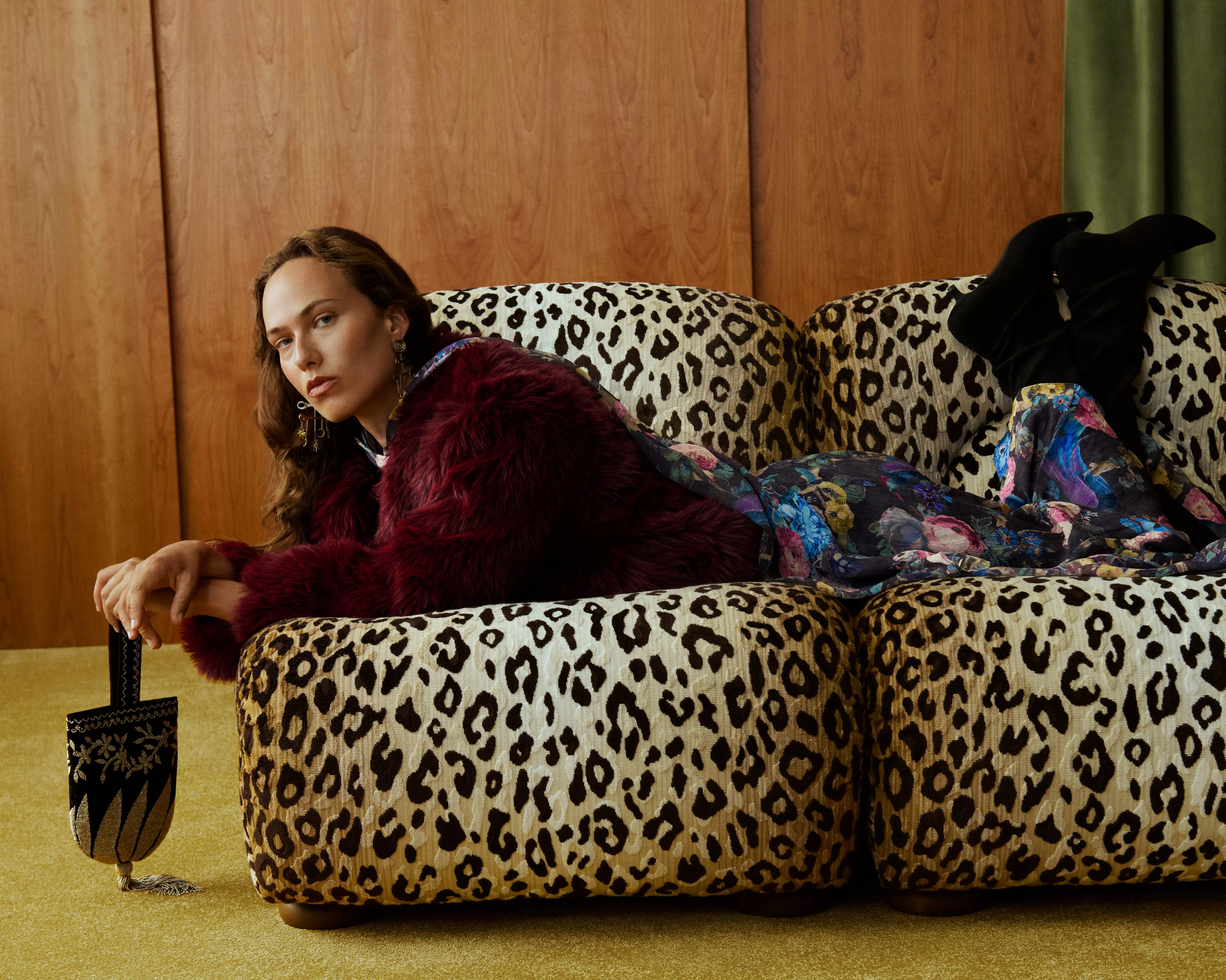 Fashion model lounging on leopard print sofa, wearing burgundy faux fur jacket and floral dress indoors
