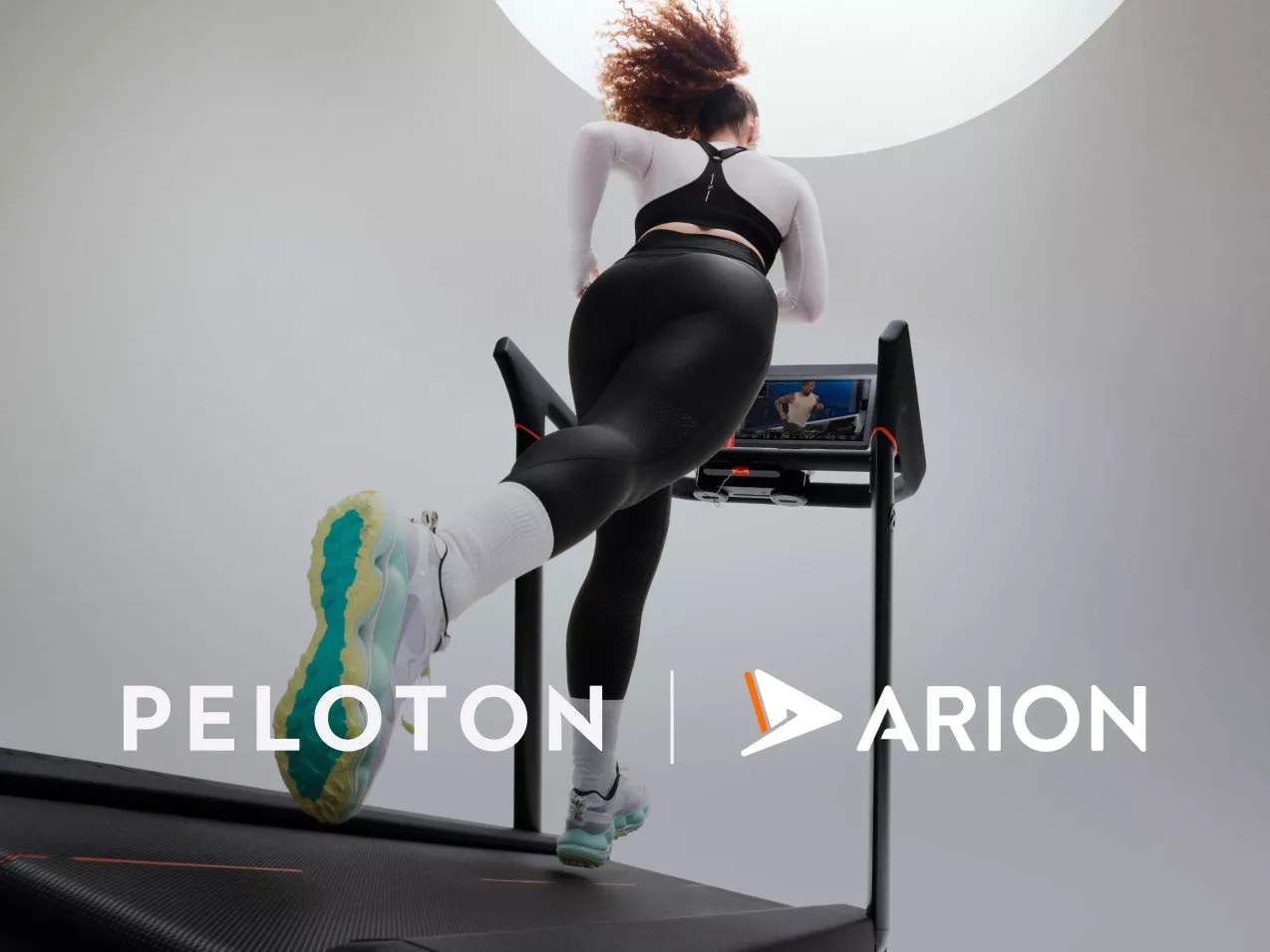 Runner using Peloton Arion treadmill with on-screen coaching, rear view in modern studio gym setting